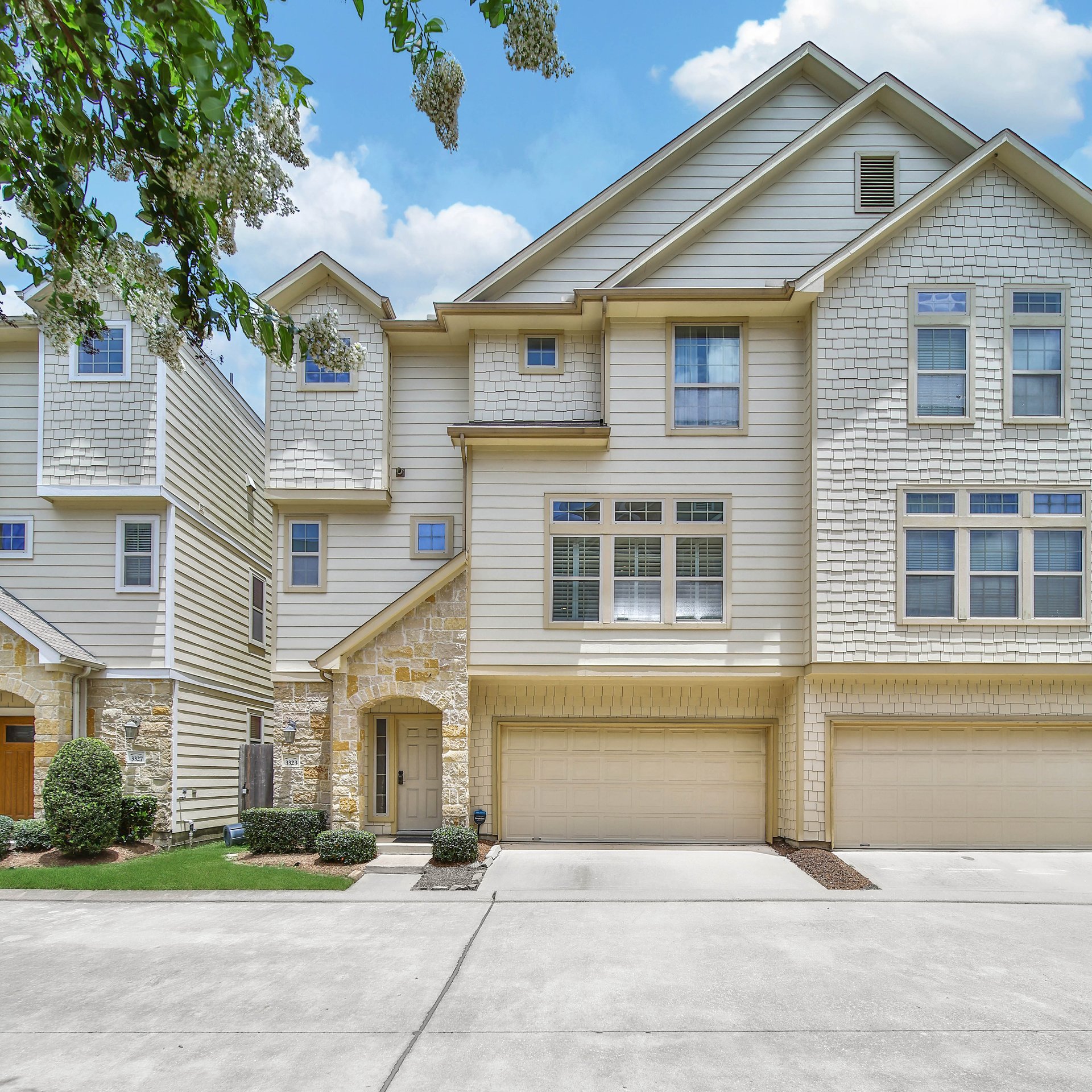 Attached light-sided homes with stone entry details, multiple garage doors, and leafy branches overhead.