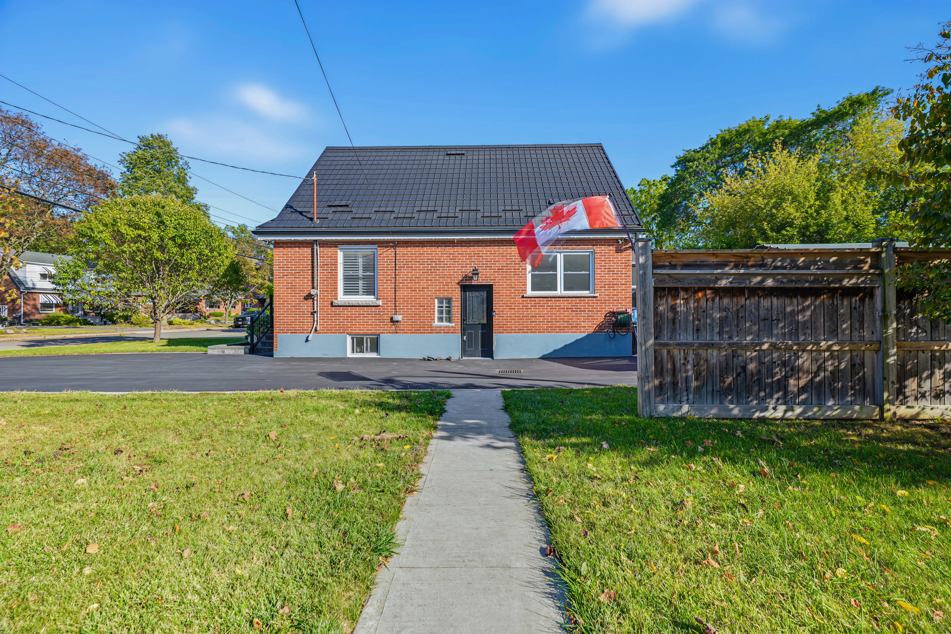 Red-brick house with a dark tiled roof and Canadian flag, viewed across the front lawn.