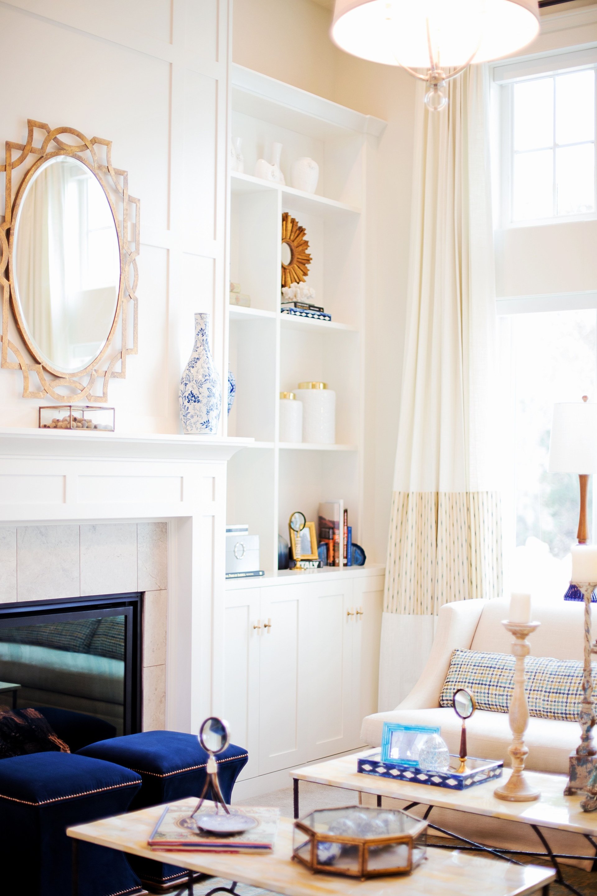 Bright living room with a tiled fireplace, white built-ins, and navy ottomans.