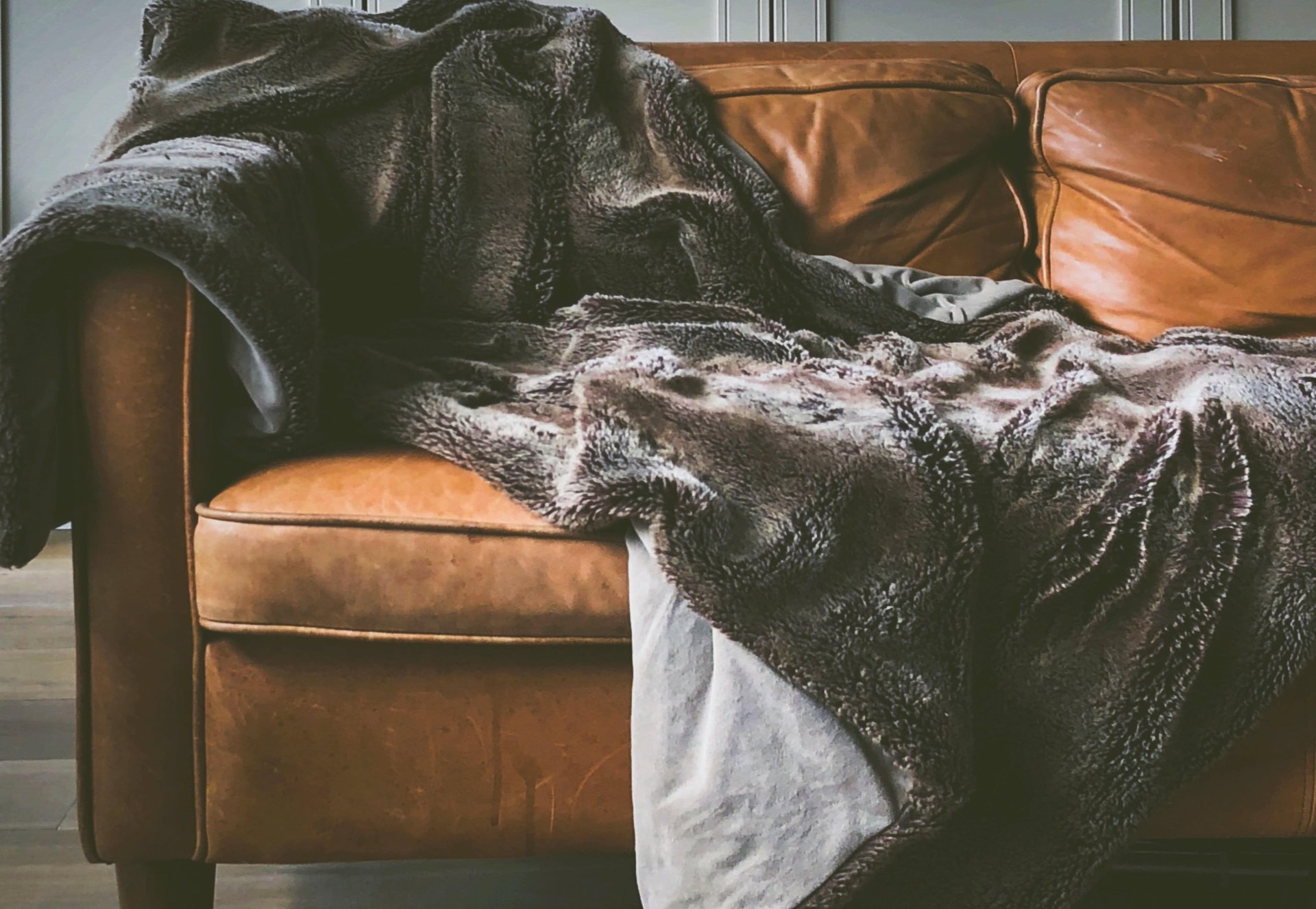 Brown leather sofa layered with a thick charcoal patterned throw and a light blanket.