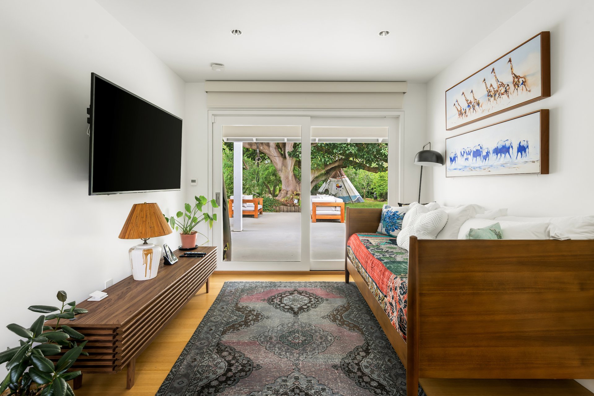 Bedroom with a wooden daybed and sliding glass doors opening onto a leafy patio.