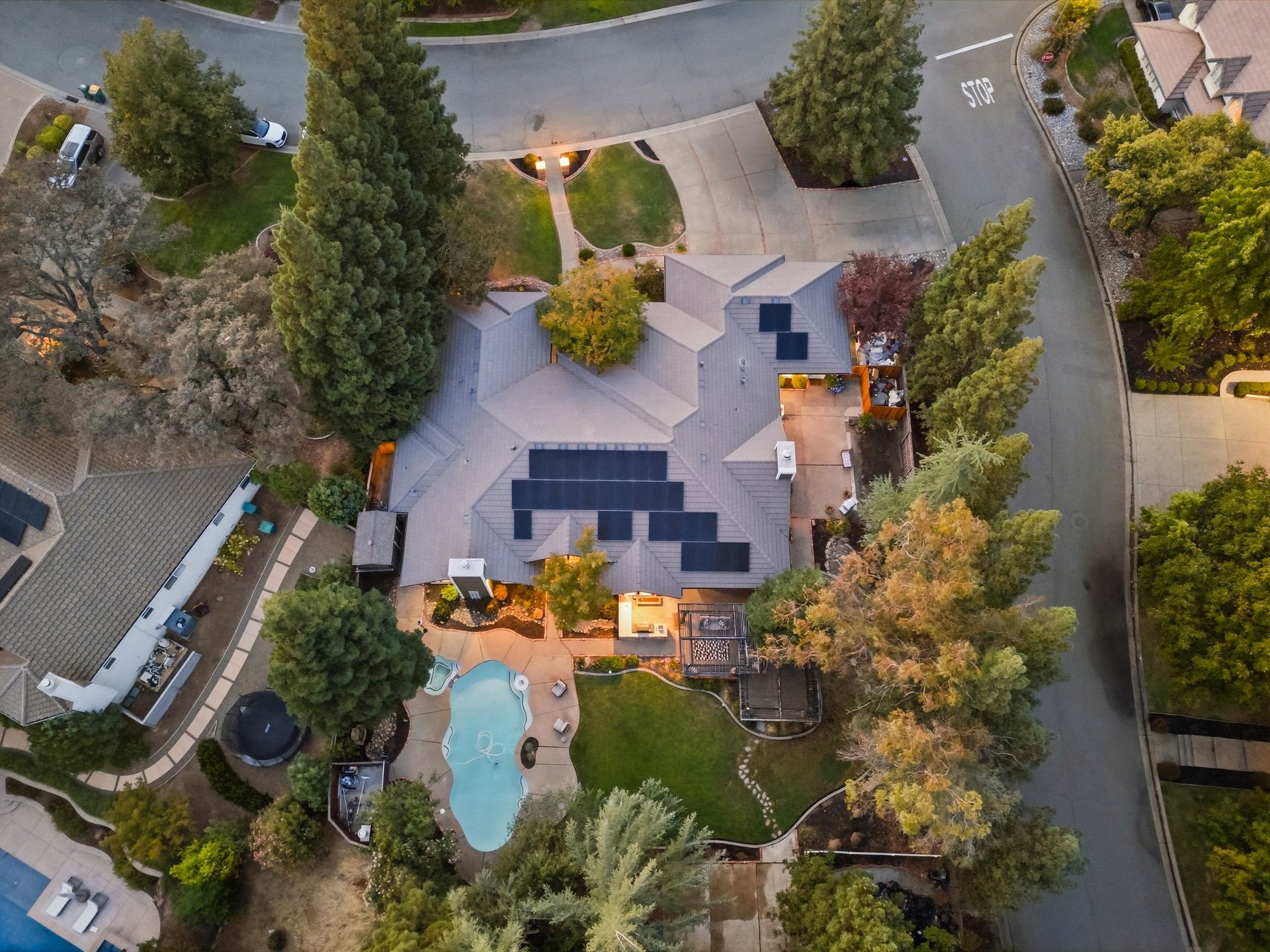 Aerial view of a home with rooftop solar panels, a swimming pool, and landscaped grounds.