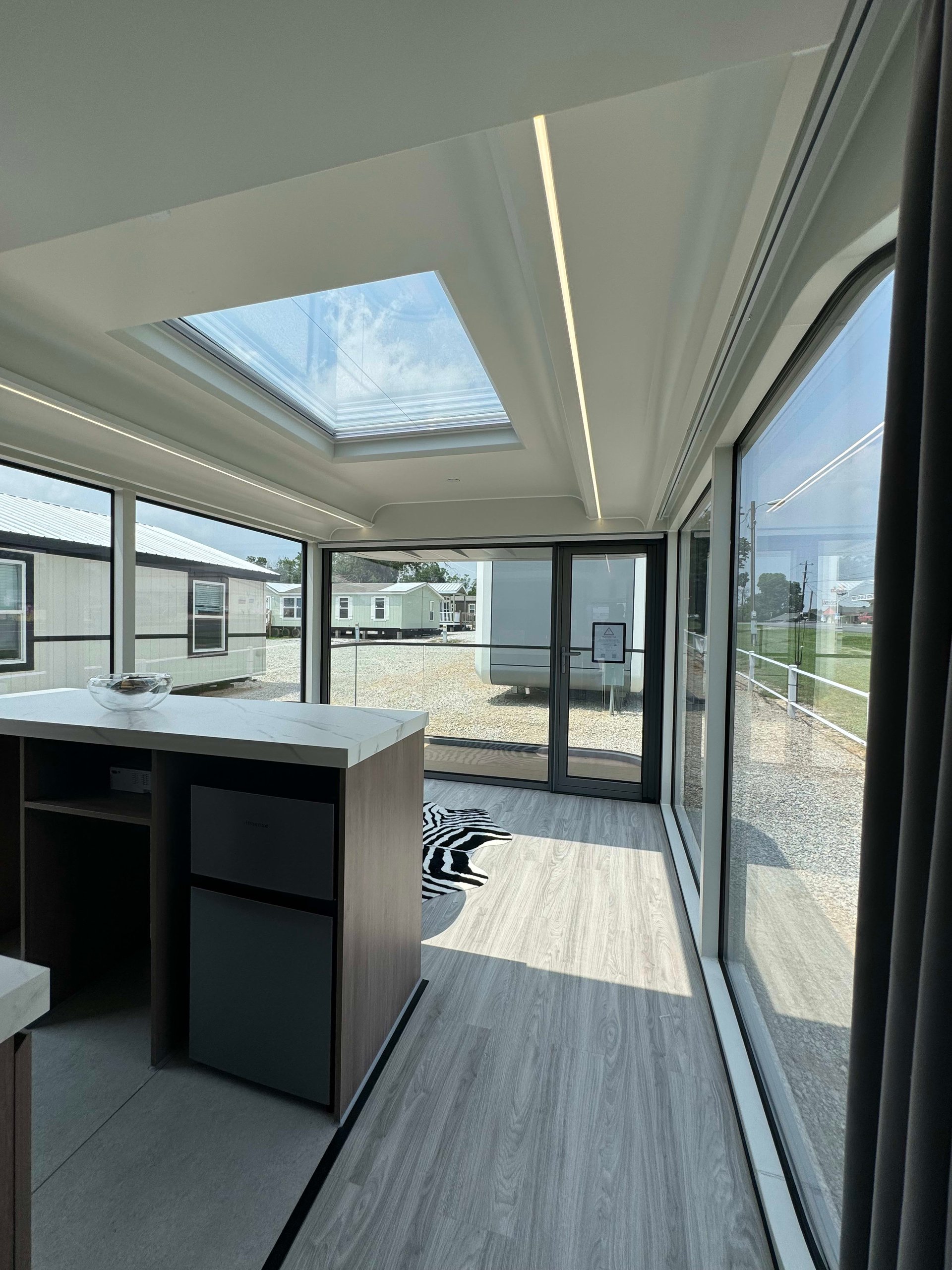 Tiny home interior with a compact kitchen island, floor-to-ceiling windows, and a large skylight.