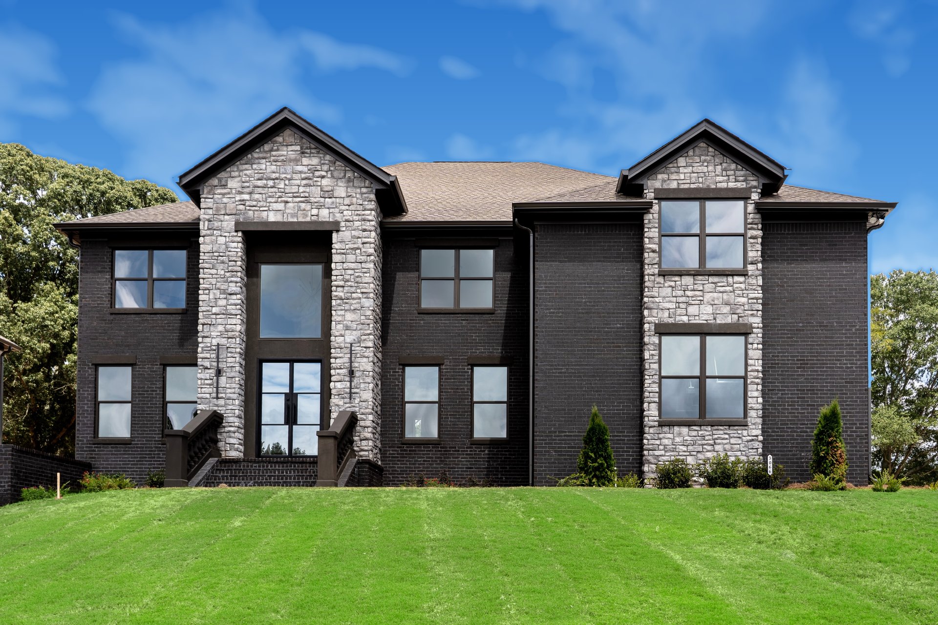 Two-story dark brick house with stone gables and a broad green lawn.