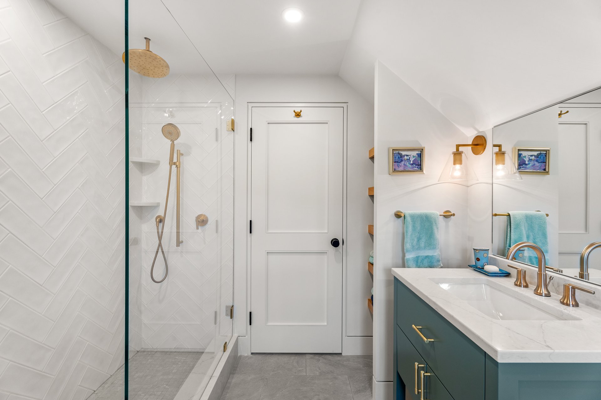 Bathroom with a glass shower, white herringbone tile, teal vanity, and brass fixtures.
