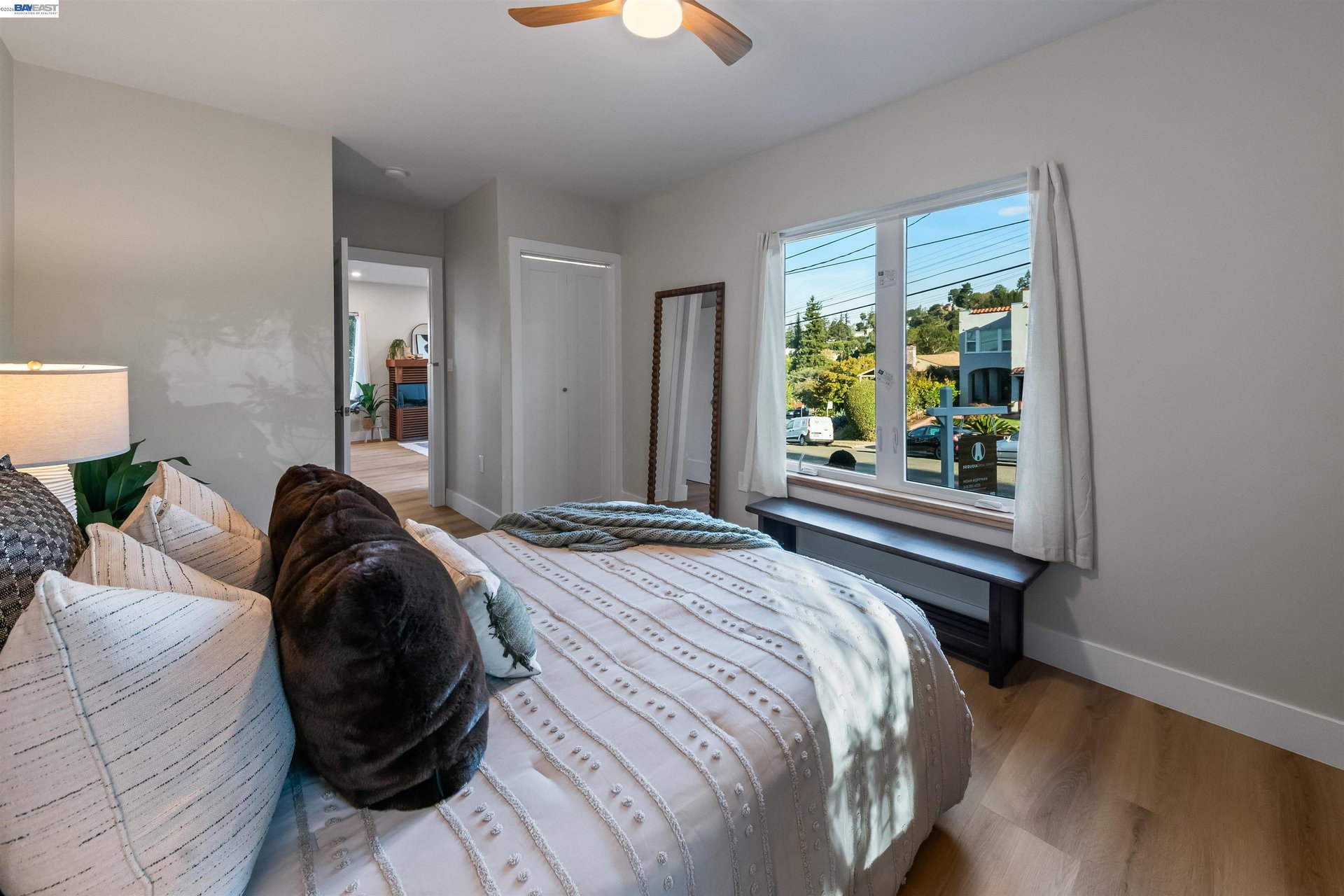 Furnished bedroom with white patterned bedding and a large window overlooking the street.