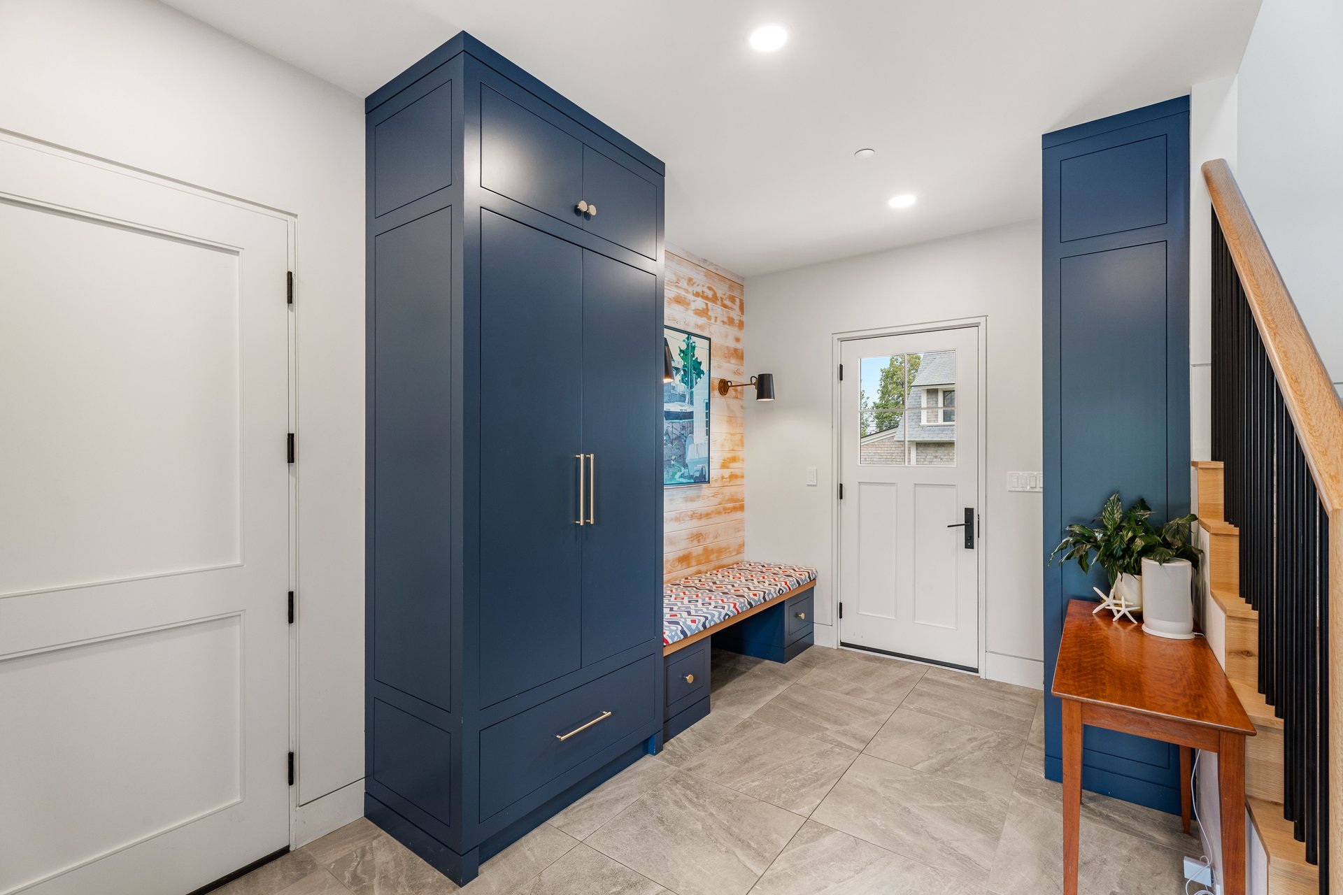 Entryway with navy built-in cabinets, a patterned bench, and a staircase with a wood handrail.