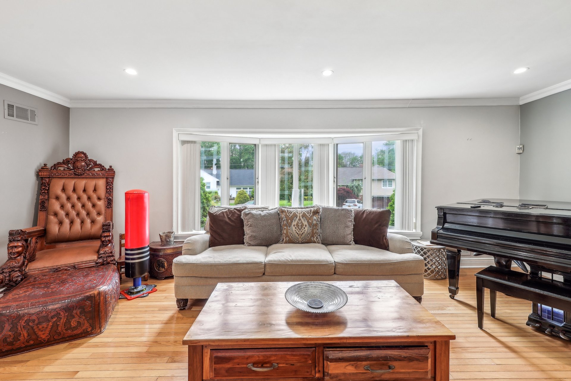Living room with an ornate carved leather chair, grand piano, and wide window.
