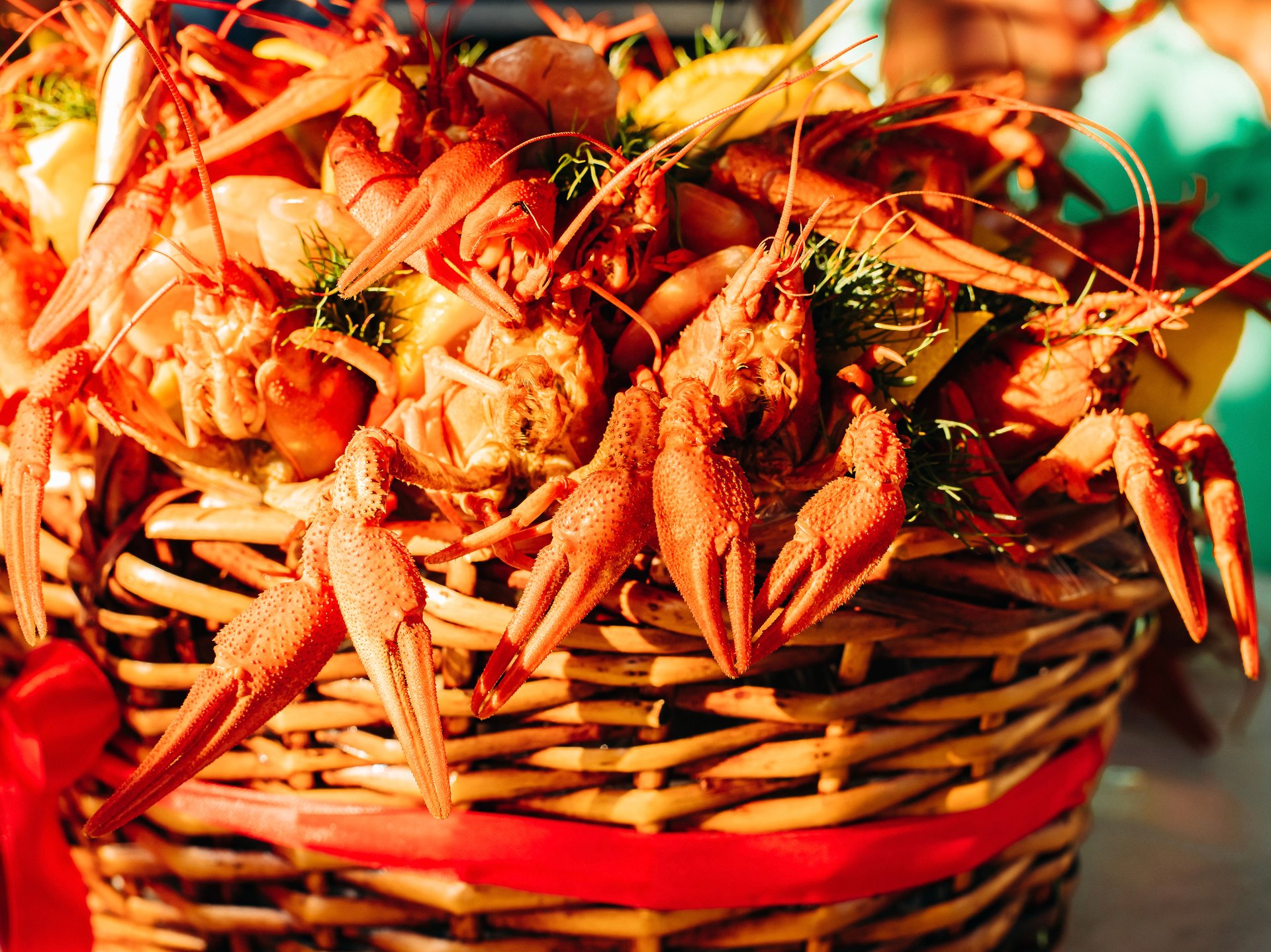 Orange-red crustaceans with long antennae and green herbs piled in a woven basket.
