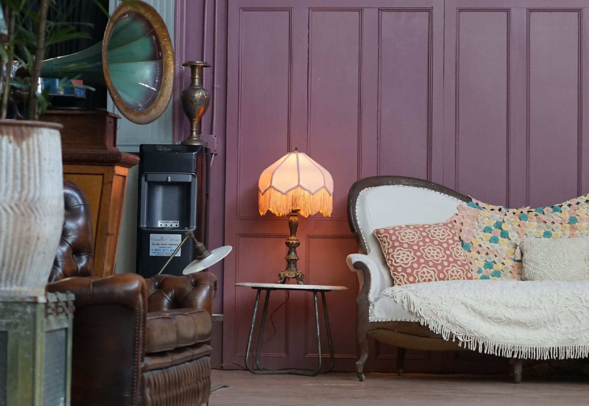 Eclectic living room with a mauve paneled wall, white settee, leather armchair, and glowing fringed lamp.