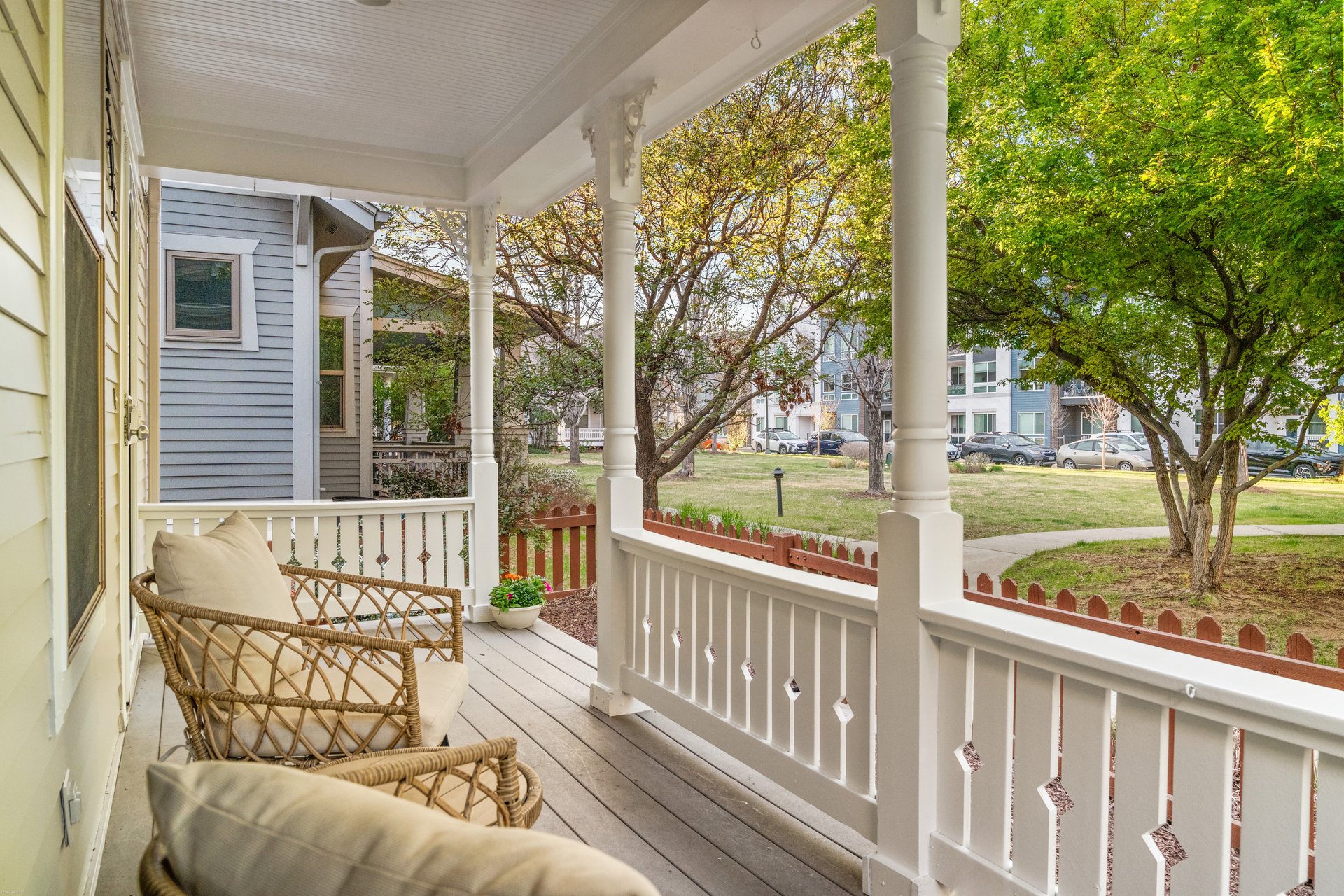 Covered front porch with wicker chairs, white railings, and leafy trees beyond.