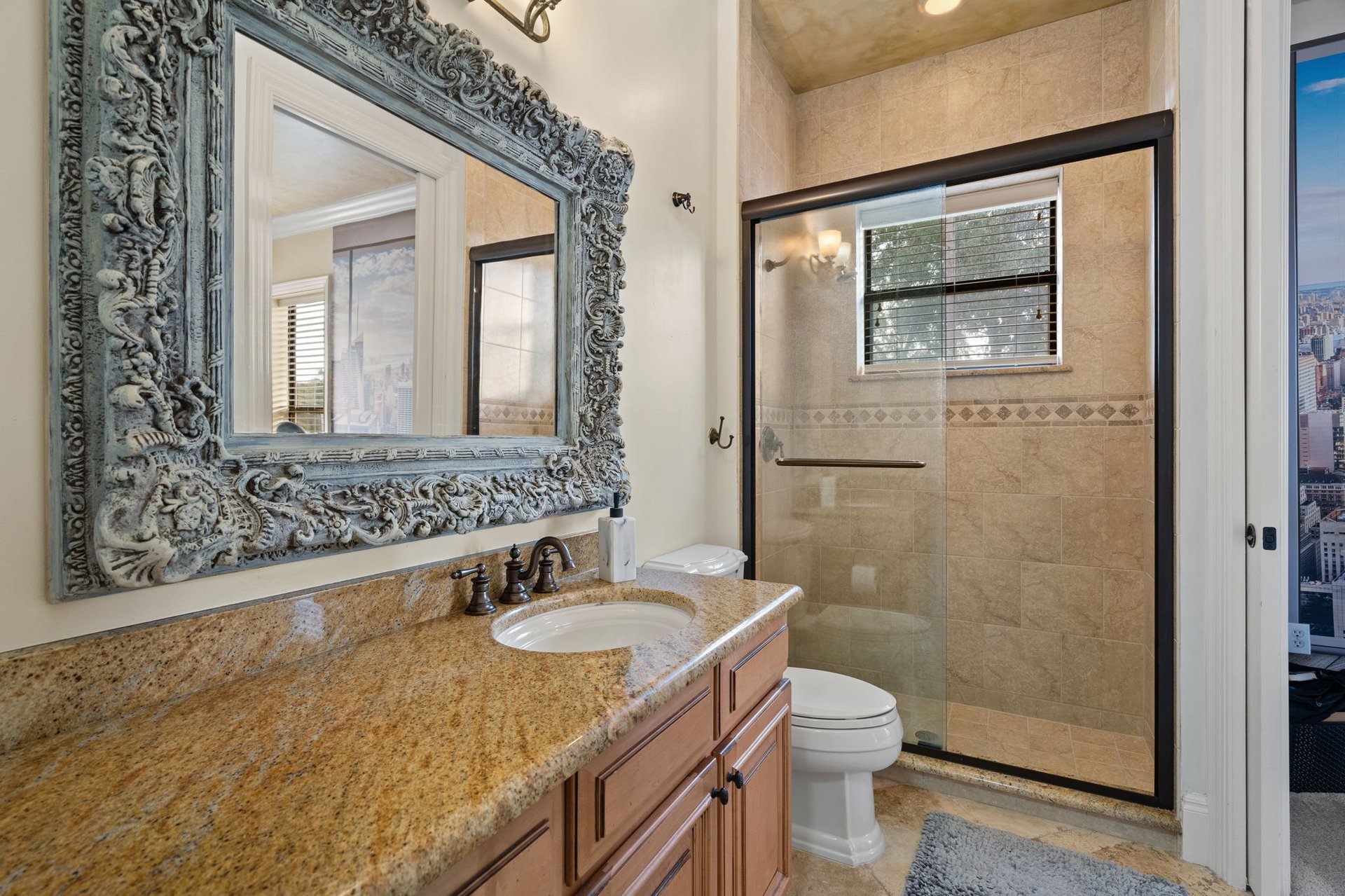 Bathroom with ornate mirror, granite vanity, and beige tiled walk-in shower.