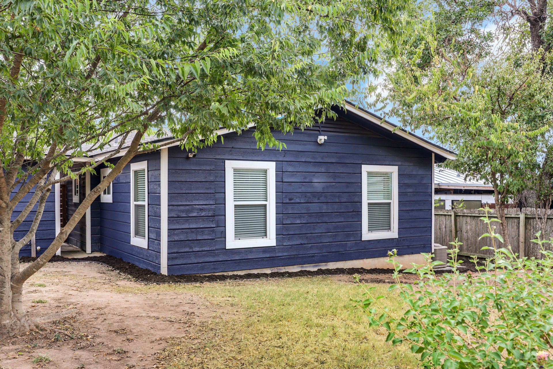 Navy-sided home with white-trimmed windows beneath leafy trees.