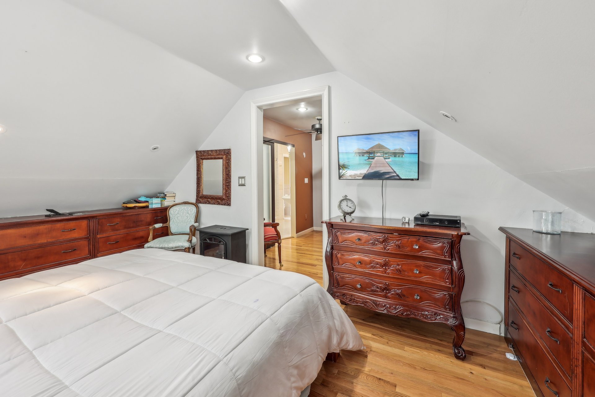 Furnished bedroom with a sloped ceiling, hardwood floors, and ornate dark wood dressers.