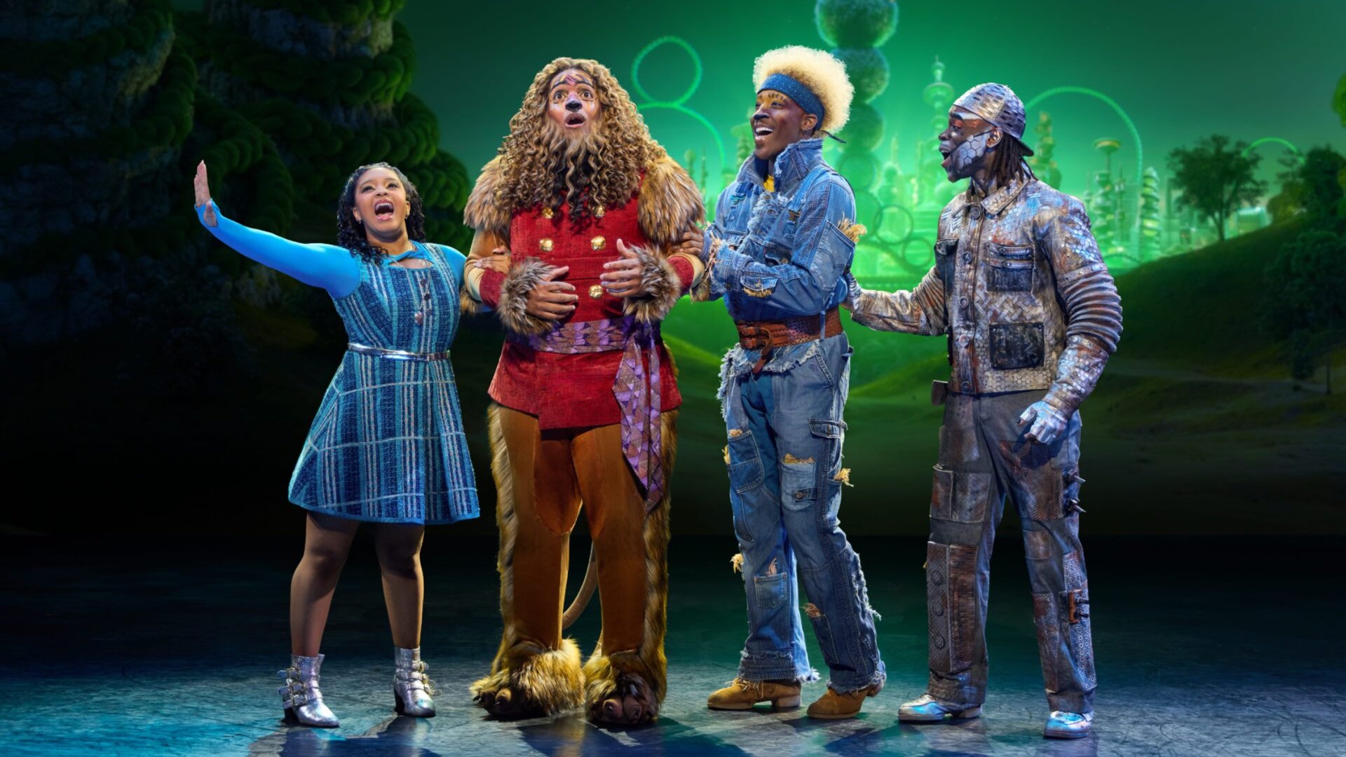 The Wiz Broadway musical cast performing at Adrienne Arsht Center in Miami with Dorothy, Cowardly Lion, and ensemble in colorful costumes on emerald-lit stage