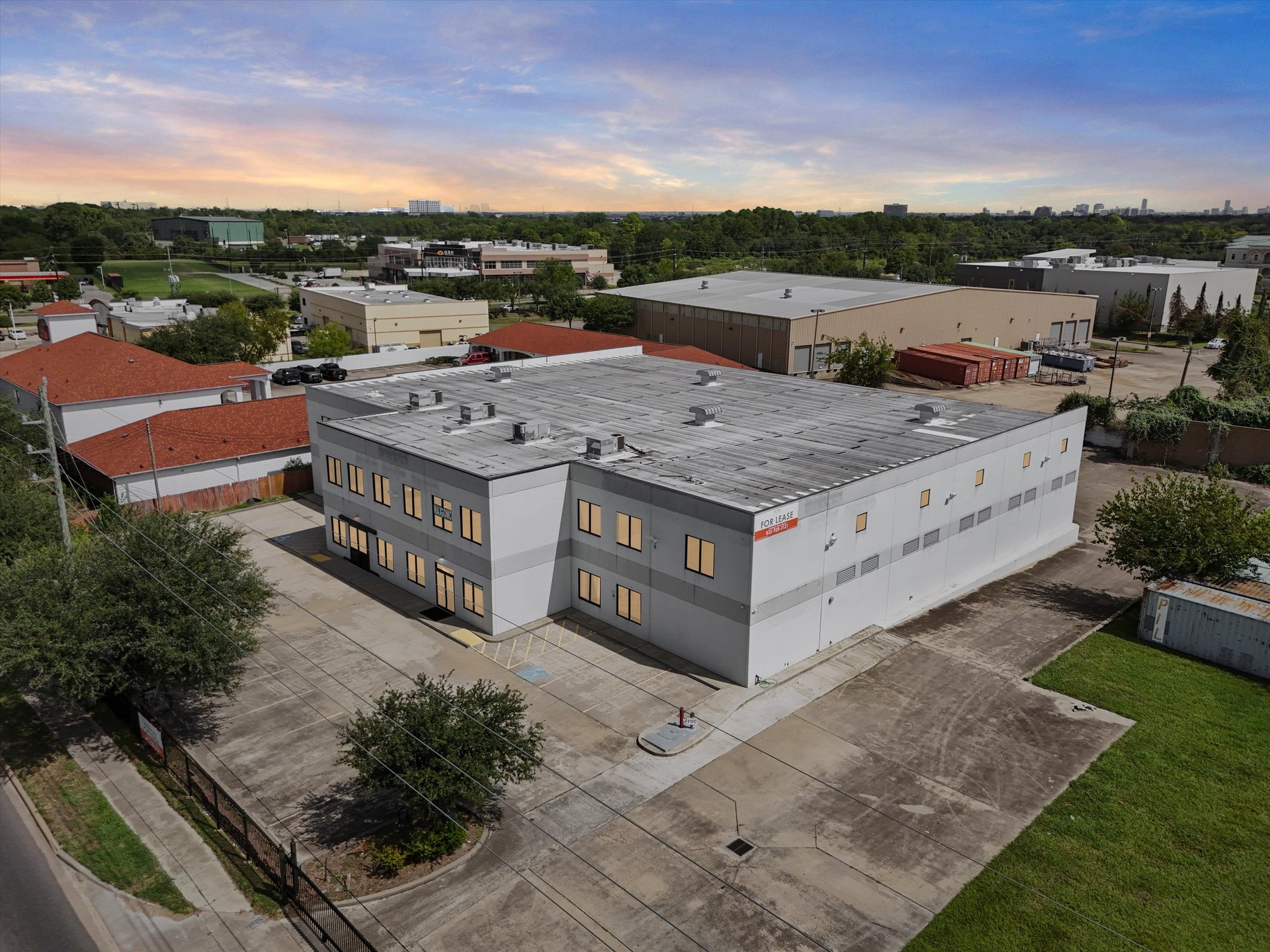 Two-story gray warehouse and office building with a large paved lot, viewed from above.
