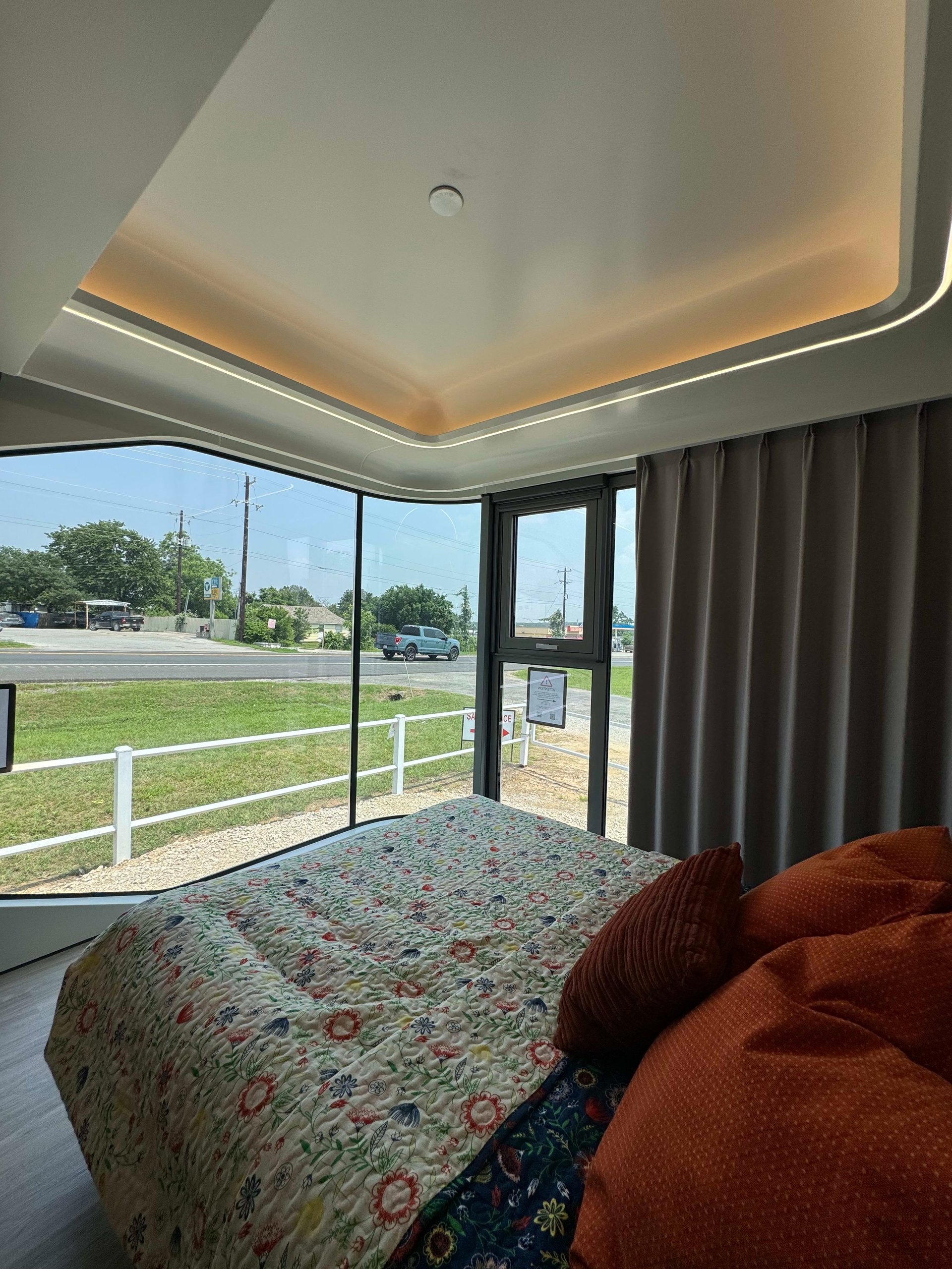 Tiny-home bedroom with a floral-quilted bed, corner windows, and warm recessed ceiling lighting.