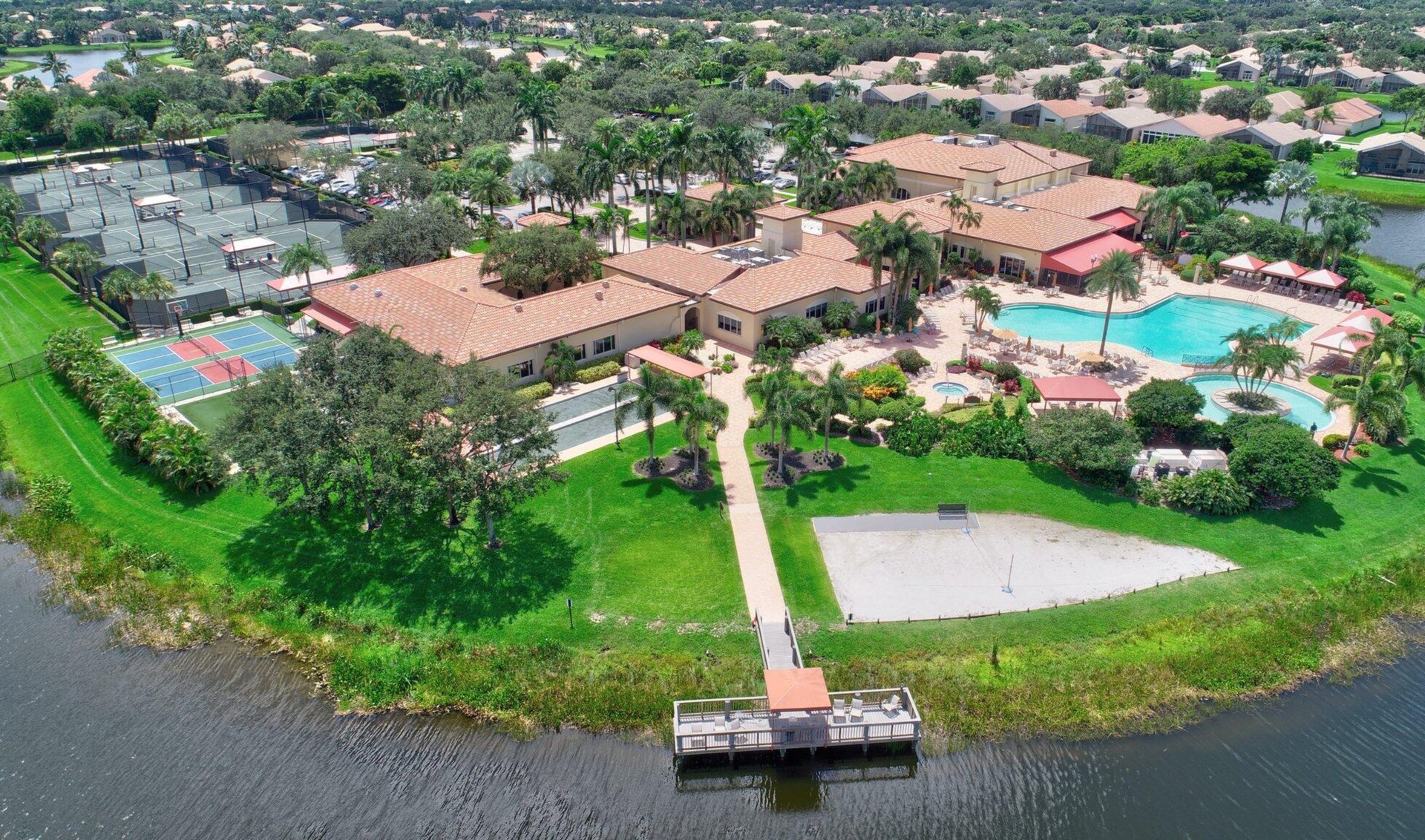 Aerial view of a country club clubhouse with a pool, tennis courts, and waterfront dock.