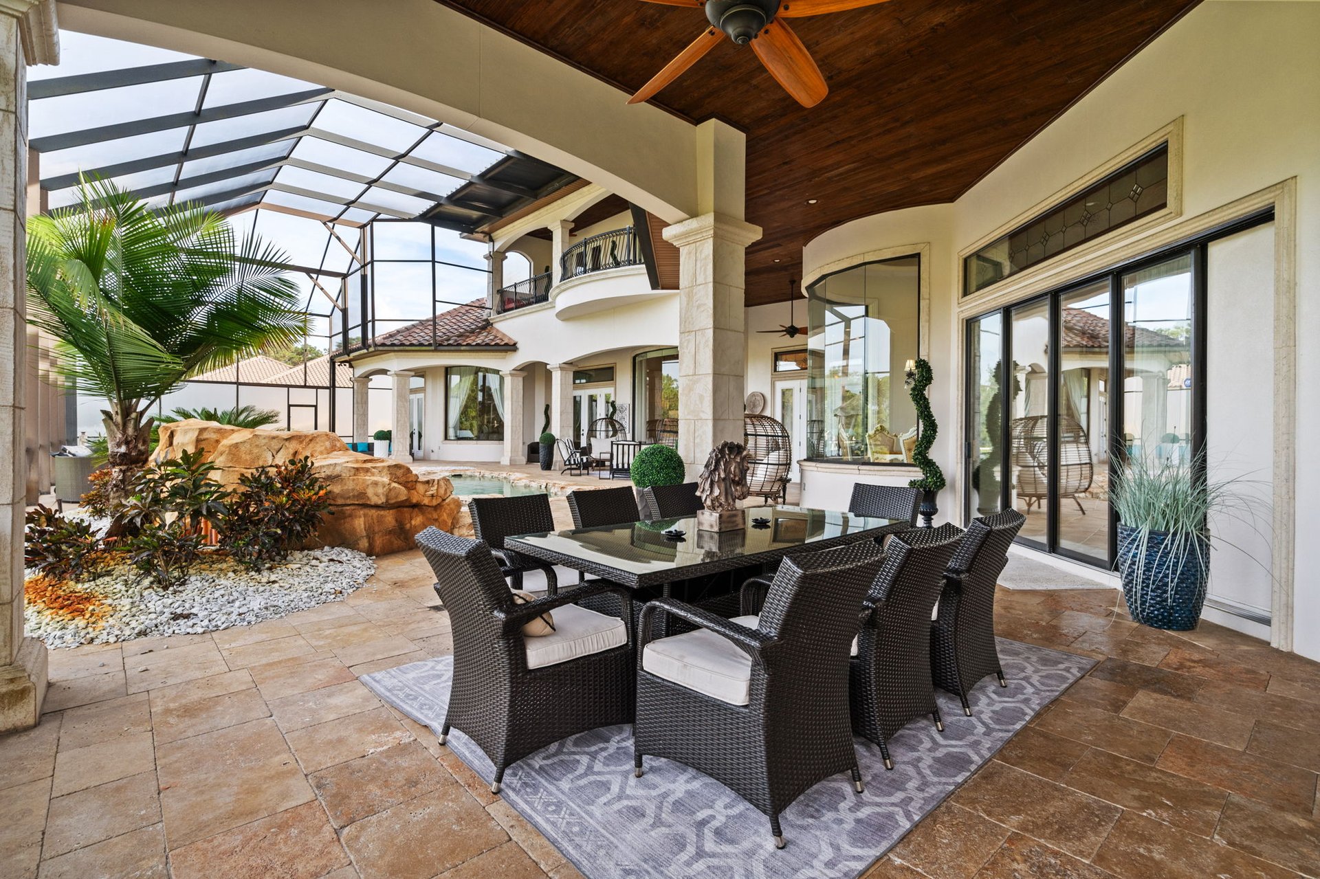 Covered patio with wicker dining set, dark wood ceiling, and screened pool area.