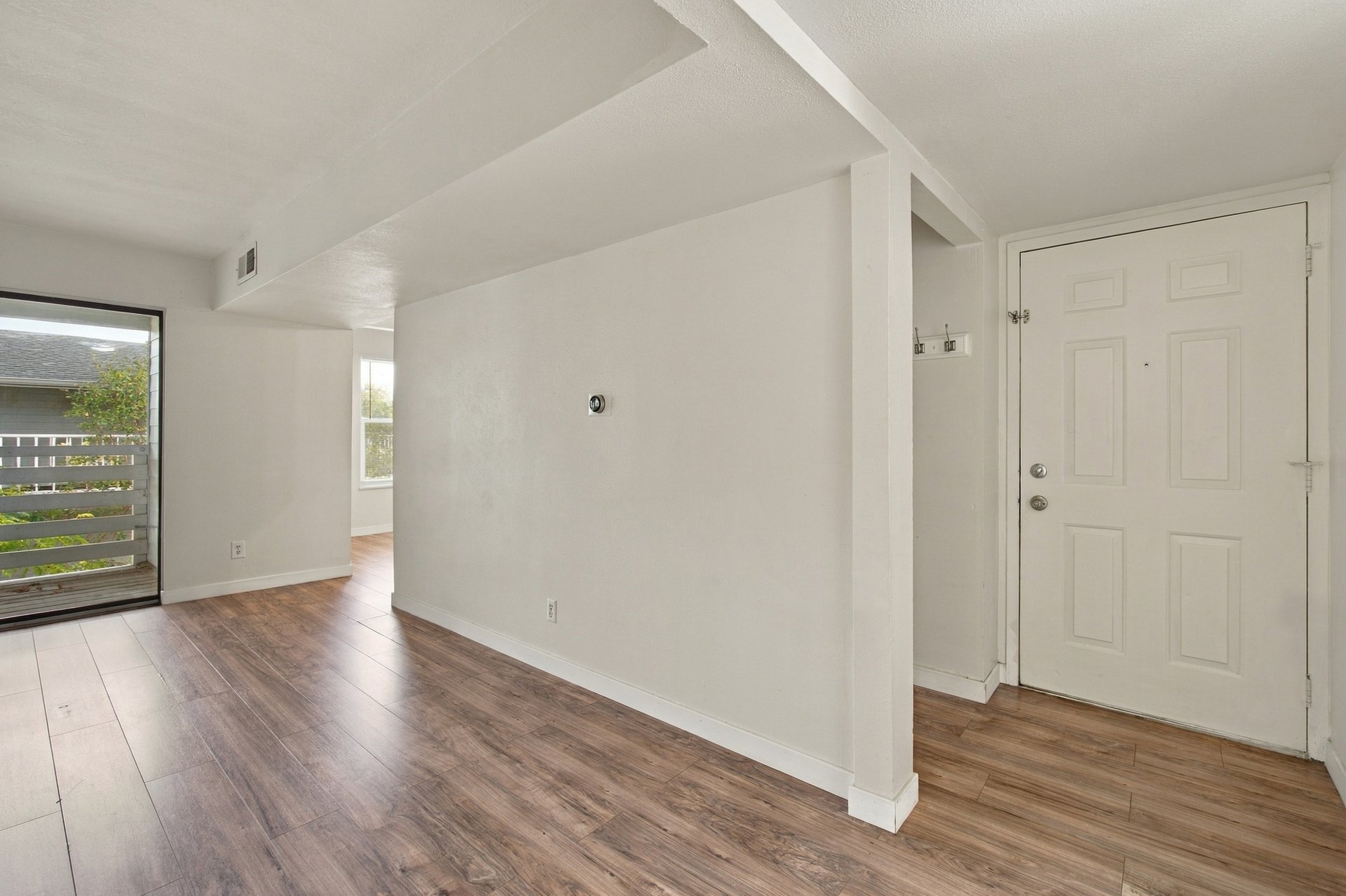 Unfurnished condo entry and living area with wood-look flooring and a sliding glass door to a balcony.