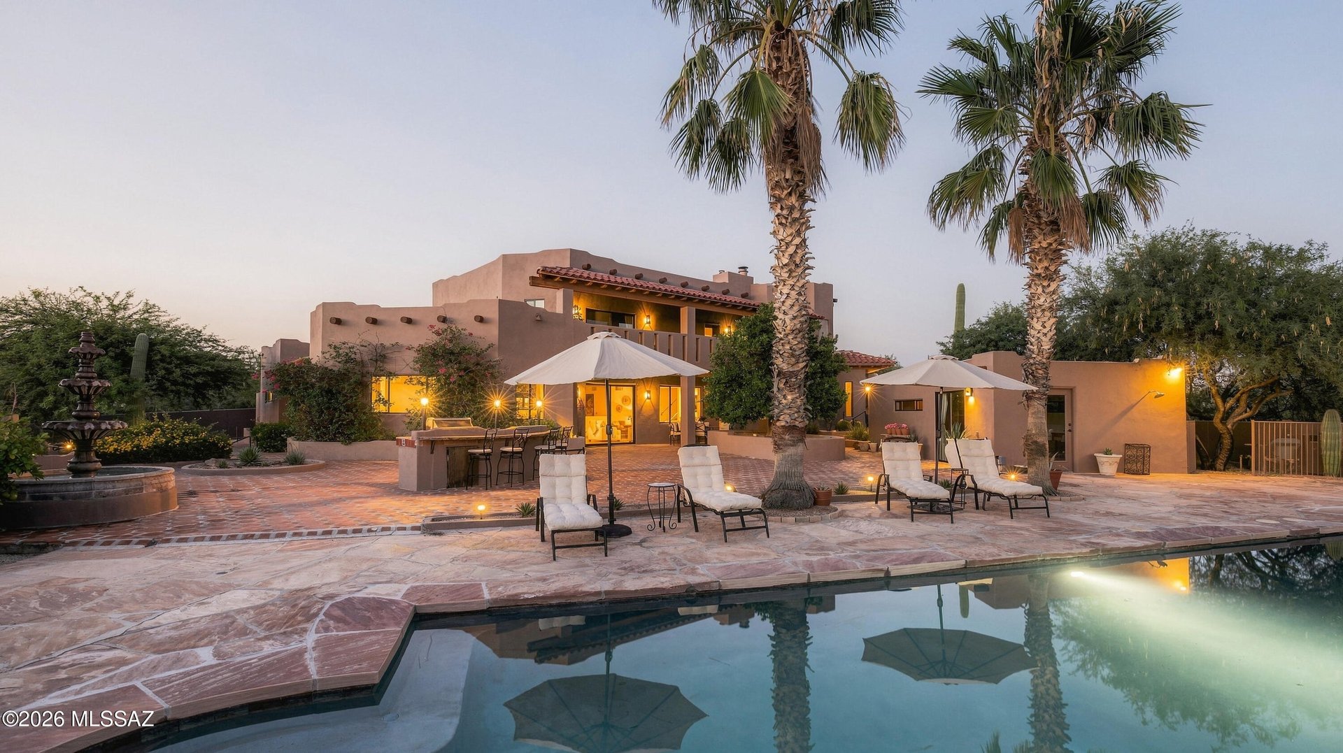 Southwestern home with a pool, palm trees, and illuminated patio at dusk.