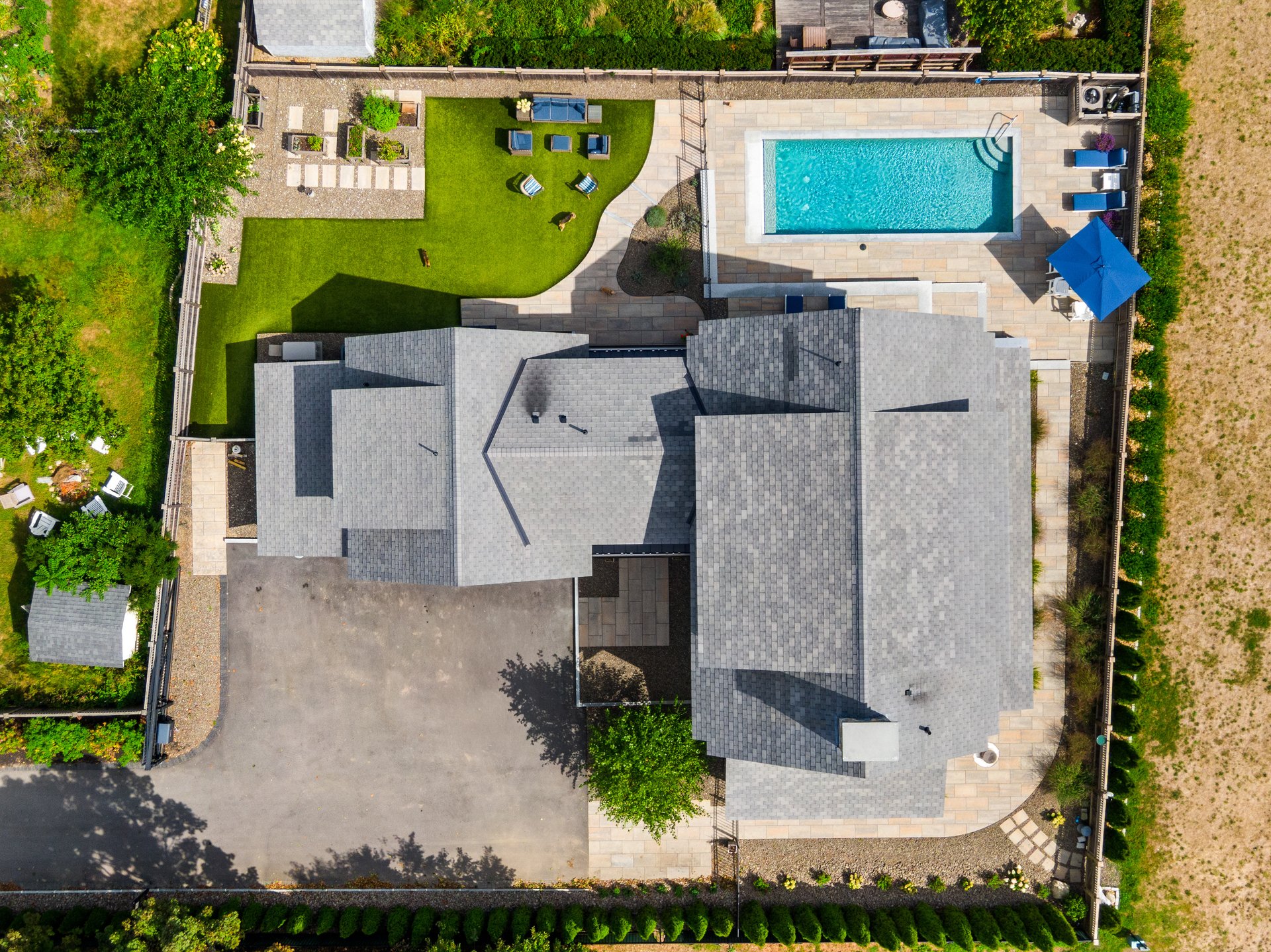Aerial view of a home with a rectangular pool, stone patio, and landscaped lawn.