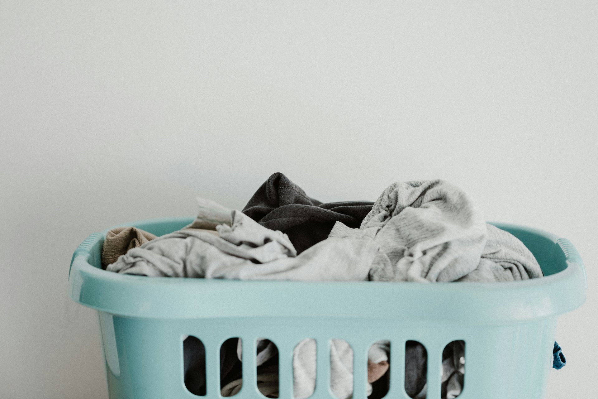 Turquoise laundry basket filled with light and dark clothes.