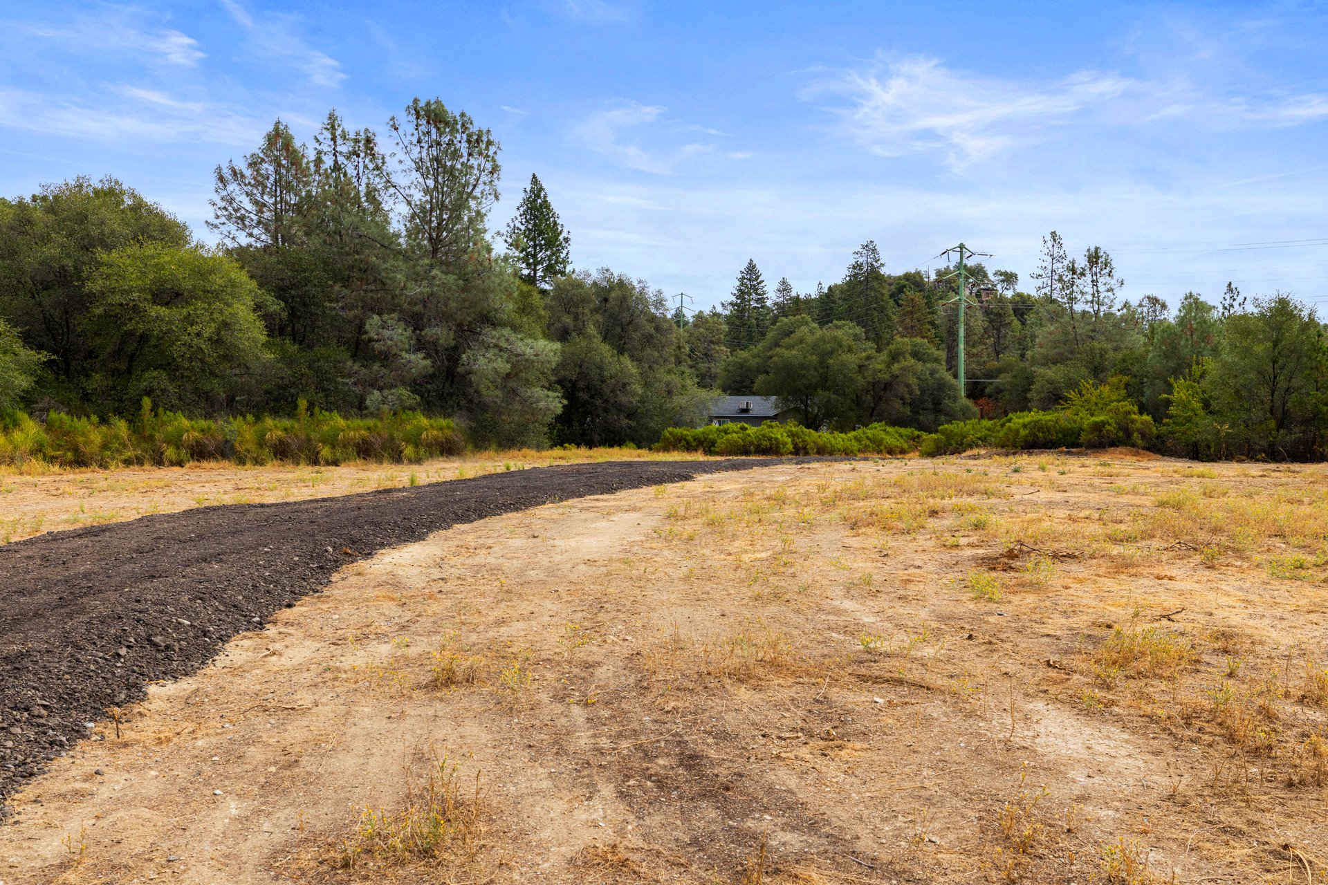 Cleared vacant lot with a curving gravel driveway and wooded edge.