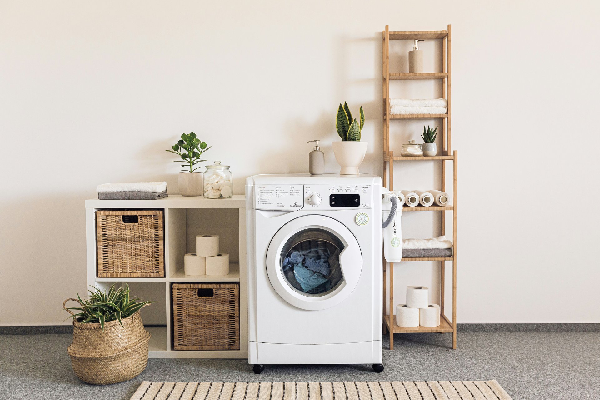 Laundry room with a front-loading washer, woven baskets, towels, and plants.