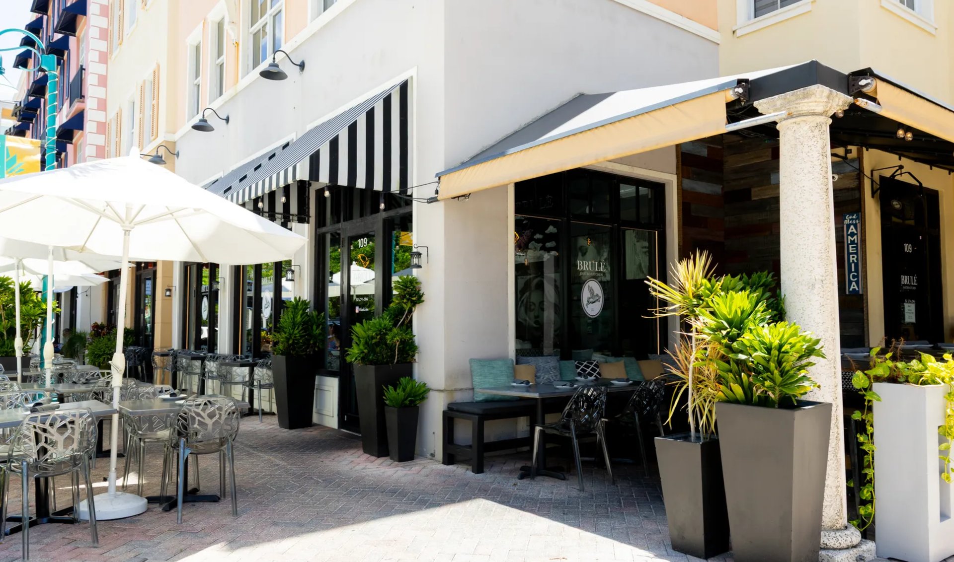 Brulé Bistro’s outdoor dining patio, shaded by white umbrellas and framed by potted tropical plants.