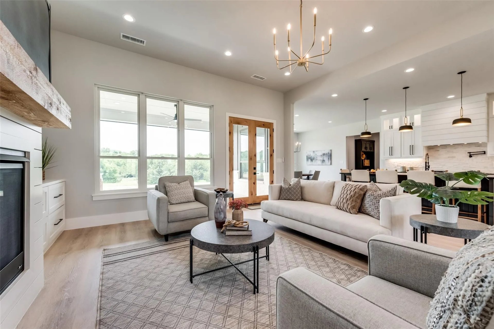 Staged living room with a fireplace, large windows, and an open kitchen.