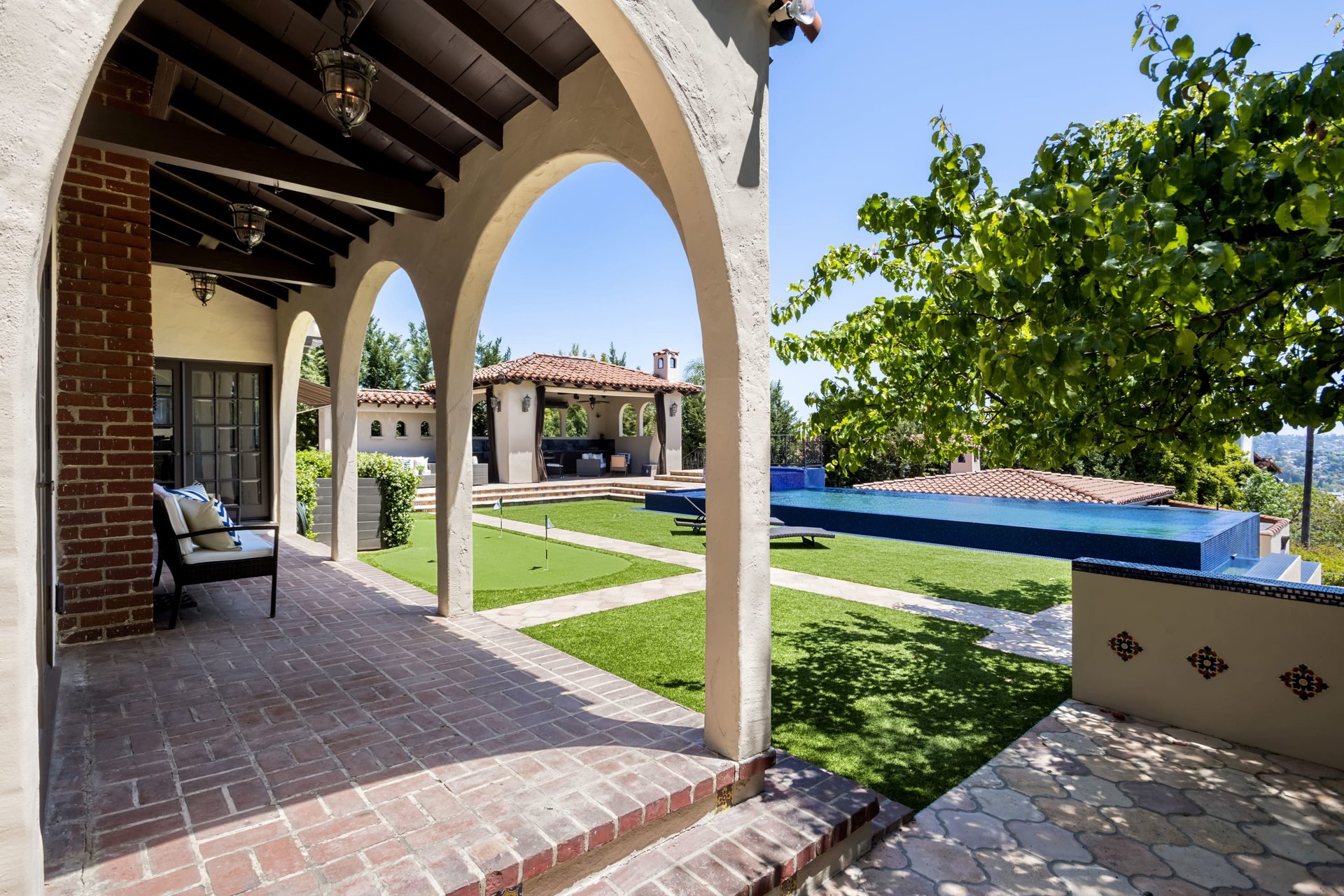 Arched covered patio overlooking a putting green and blue swimming pool.