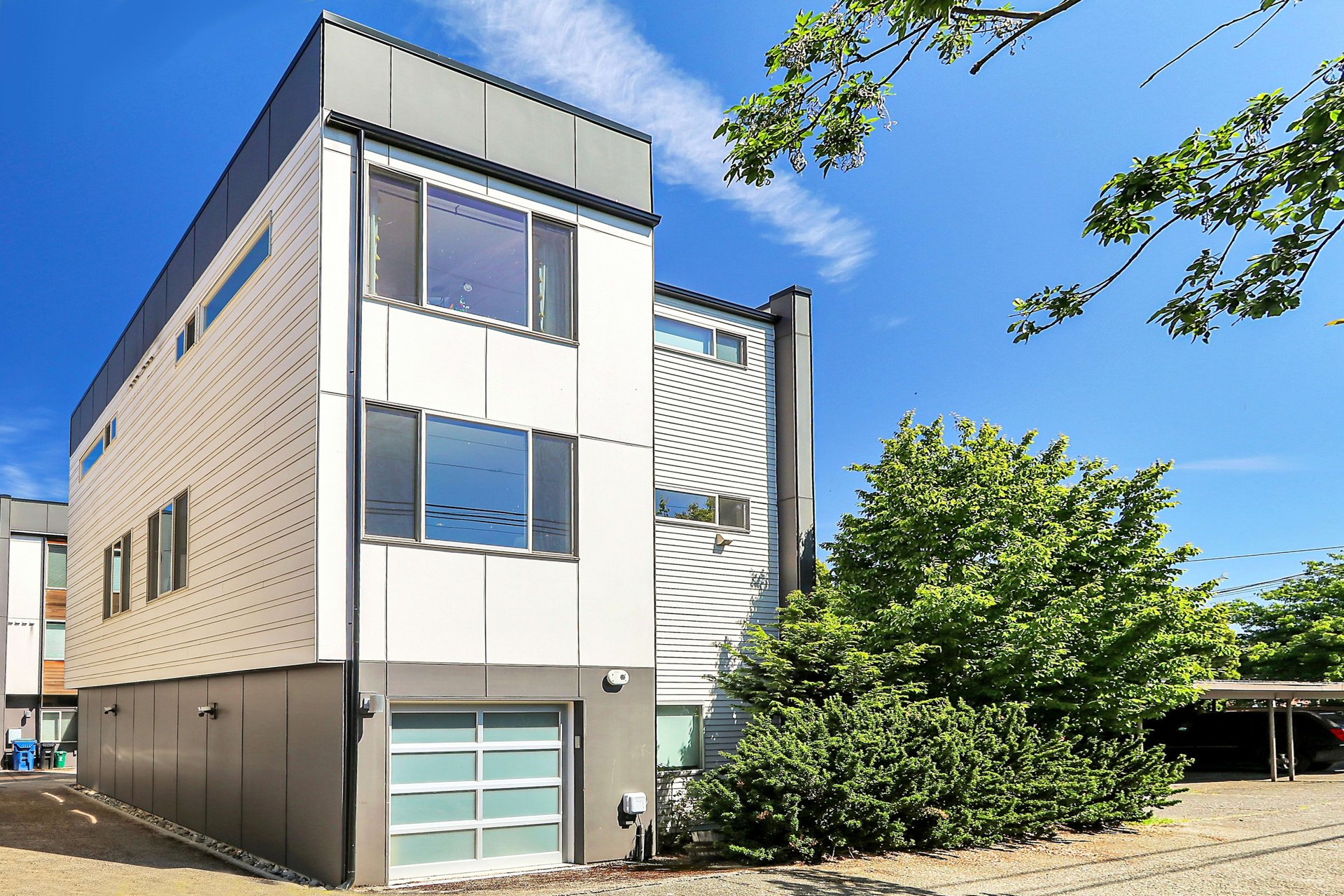 Modern multi-story home with pale siding, large windows, and an attached garage.