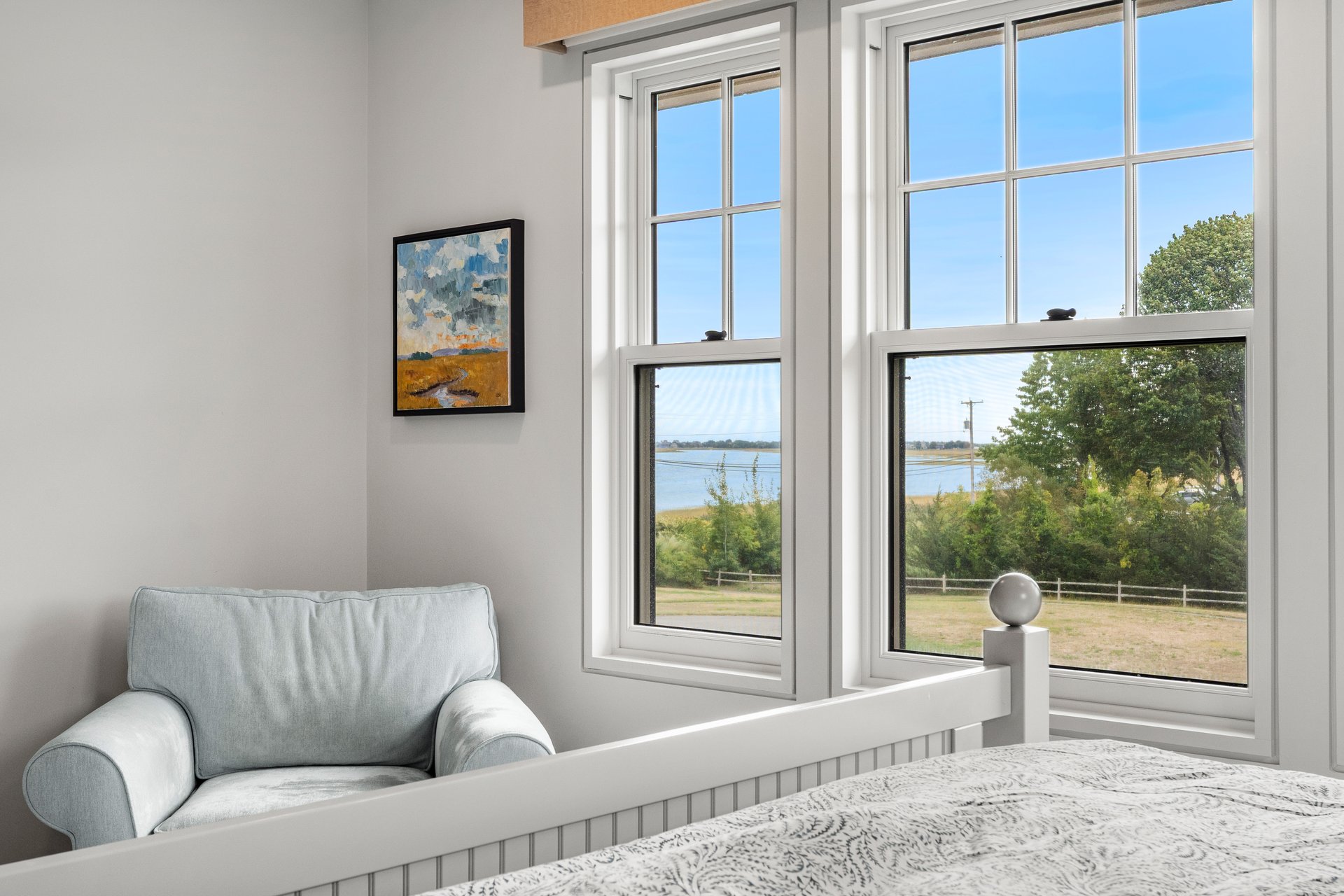 Bedroom with a pale blue armchair and large windows overlooking the water.