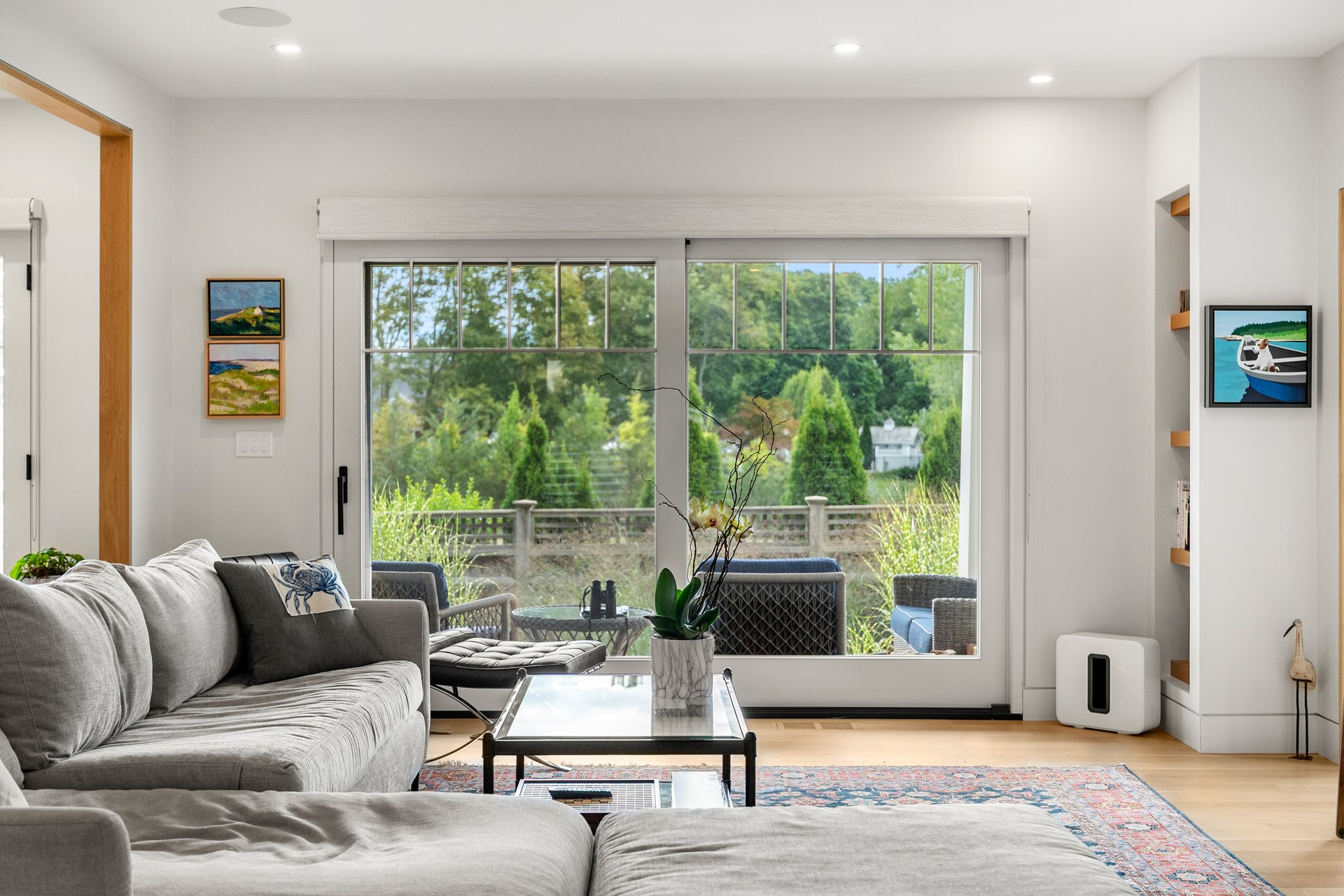 Living room with a gray sectional and large sliding doors overlooking a leafy deck and garden.