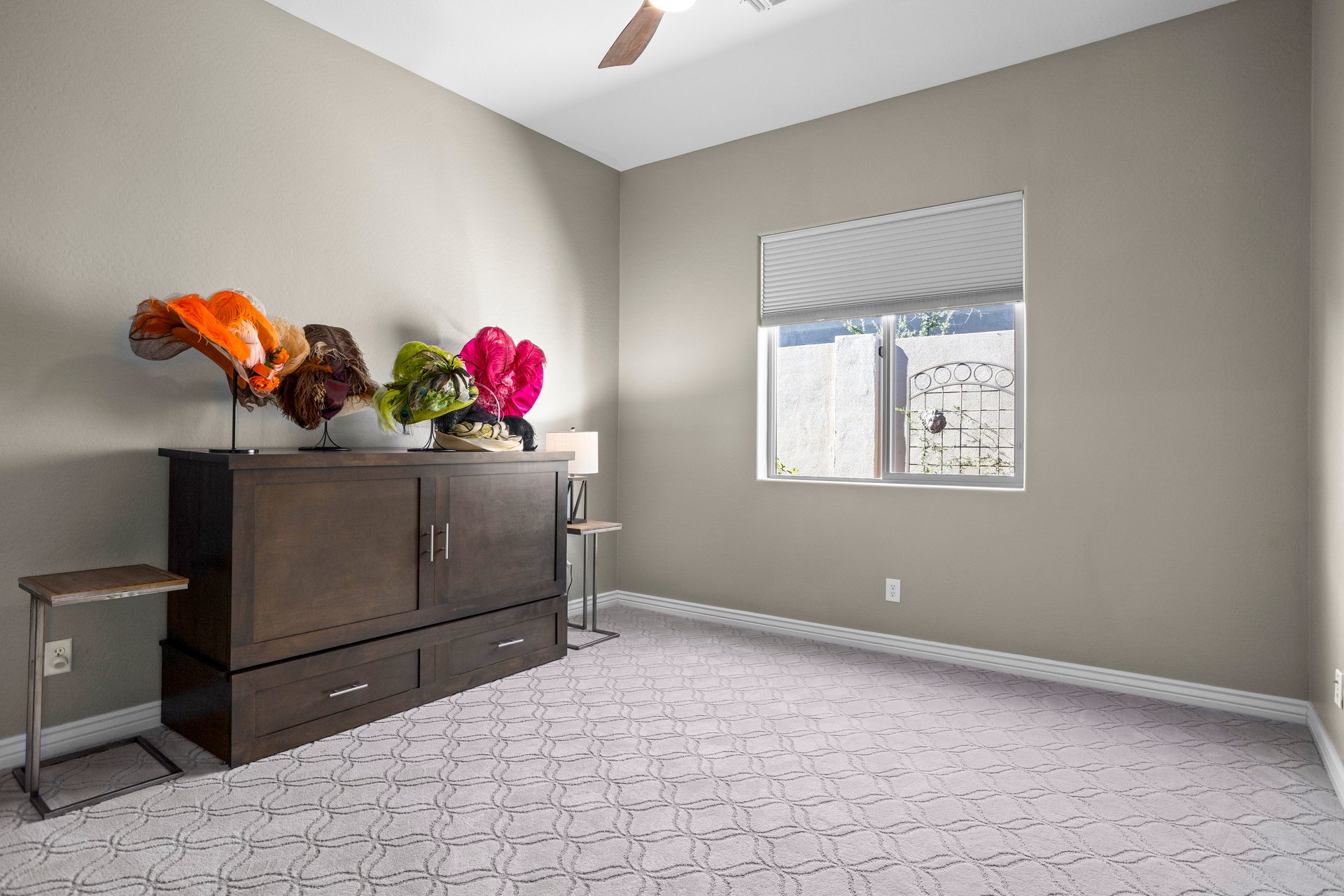 An unfurnished bedroom with a dresser, decorative hats on top, a window with a blind, and carpeted floor.