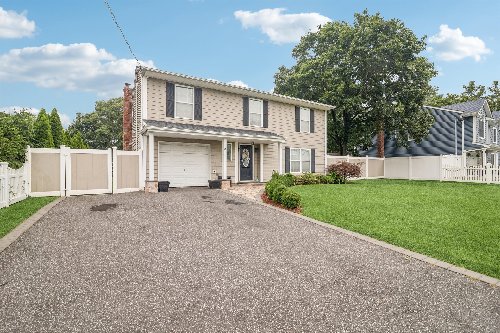 Two-story beige house with dark shutters, a wide driveway, and a fenced green yard.