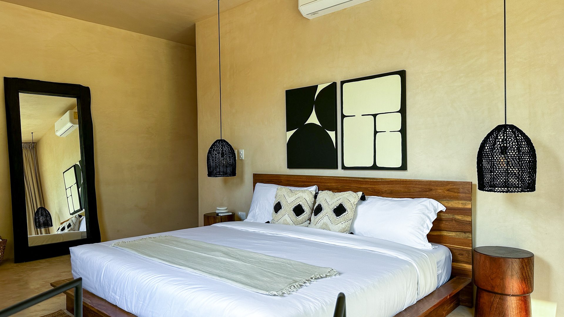 Bedroom with a large white bed, wooden headboard, woven pendant lights, and geometric wall art.