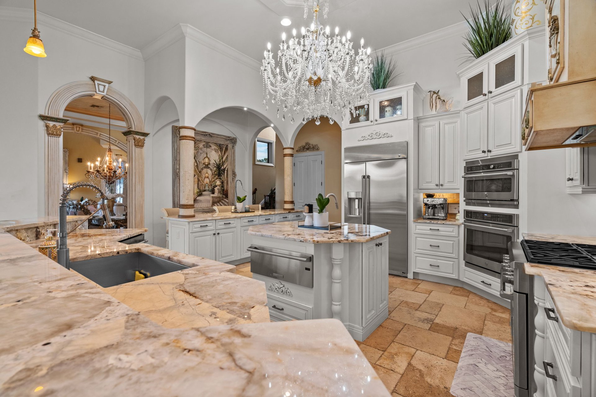 Kitchen with white cabinetry, marble island and counters, stainless steel appliances, and a crystal chandelier.