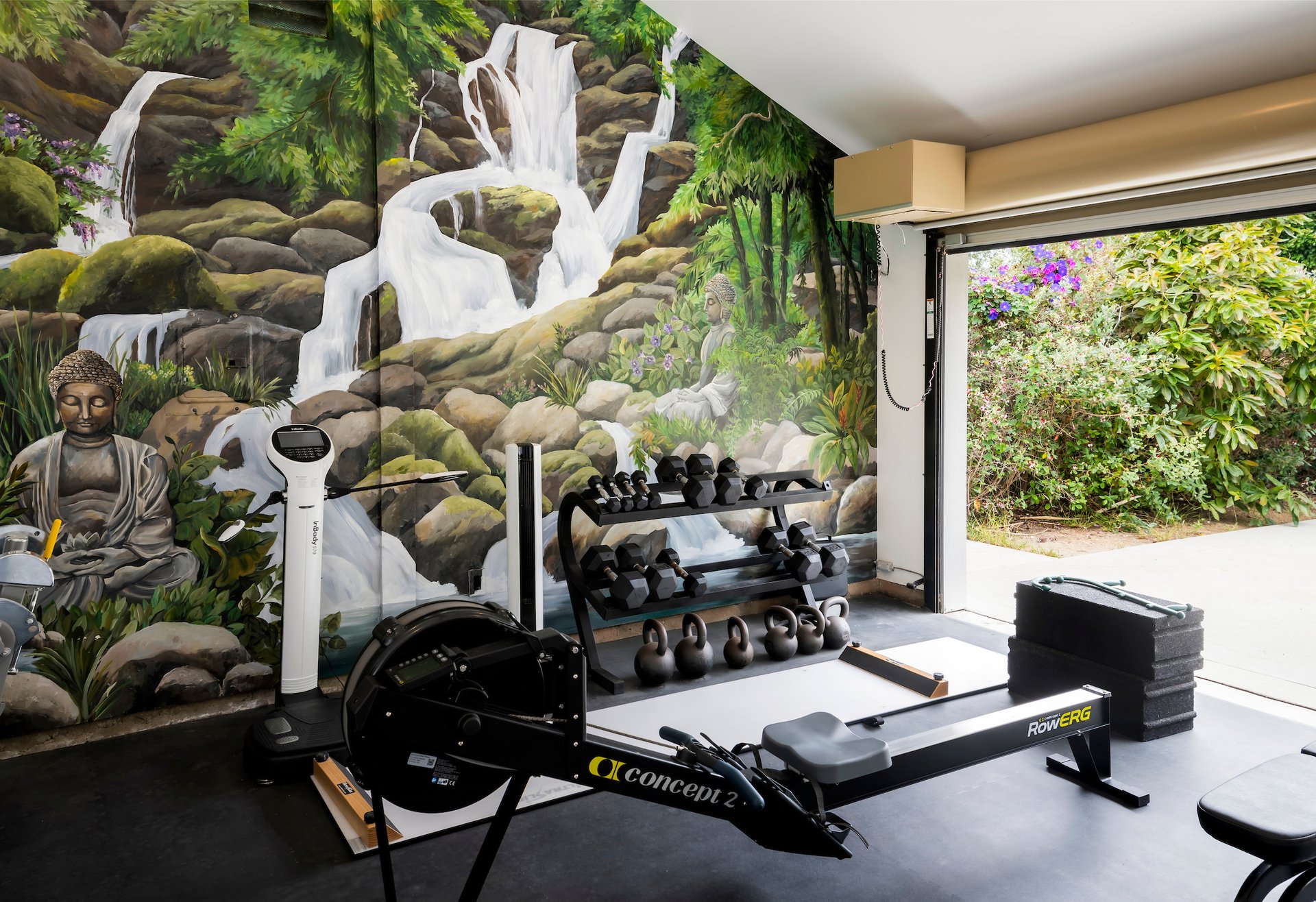 Home gym with a waterfall mural, exercise equipment, and an open garage door to the garden.