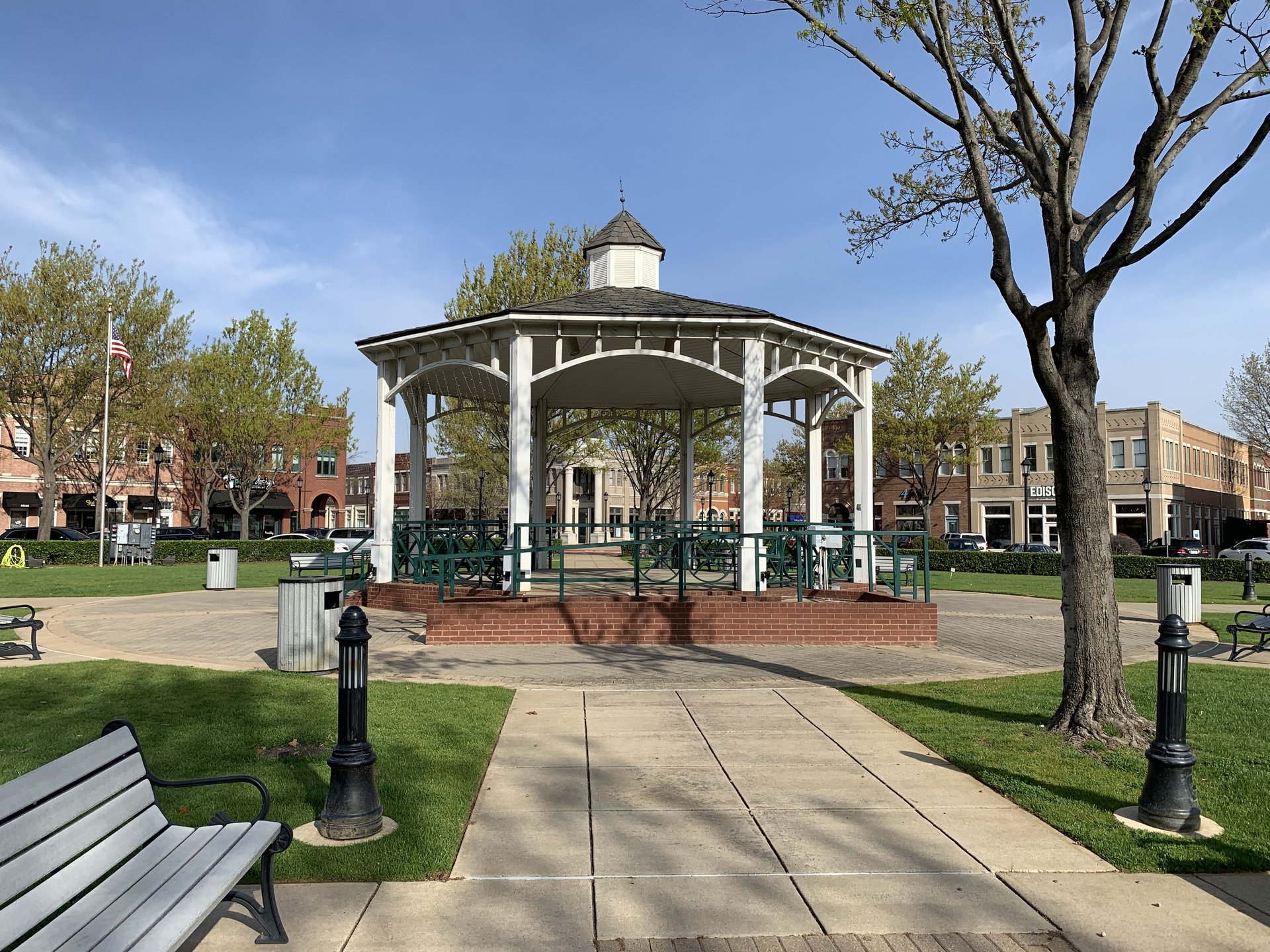 Gazebo in a town square, surrounded by benches, trees, and storefronts.