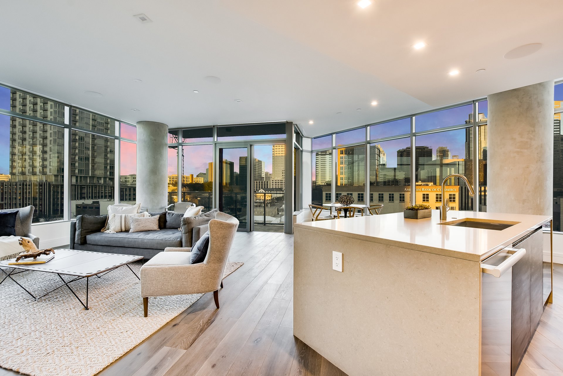 Modern condo living room and kitchen with a stone island and floor-to-ceiling windows overlooking downtown Austin.