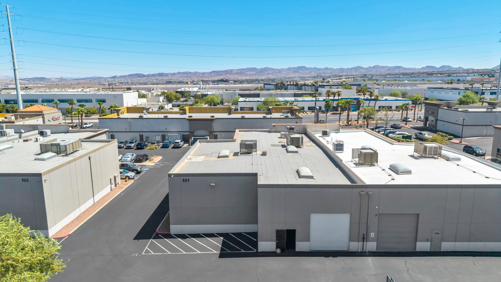 Commercial warehouse complex with flat rooftops, parking lanes, and mountains in the distance.