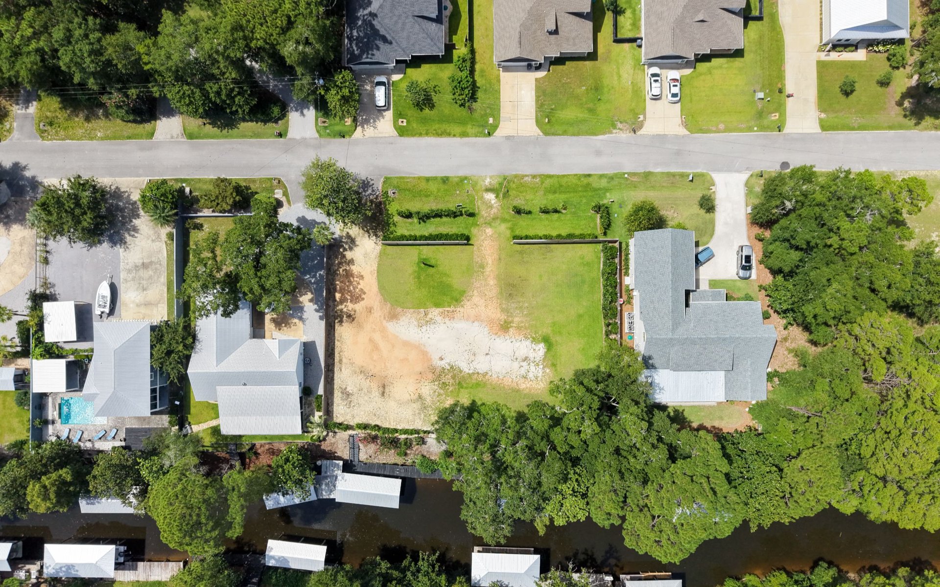 Aerial view of a vacant waterfront lot between homes, with canal access and mature trees.
