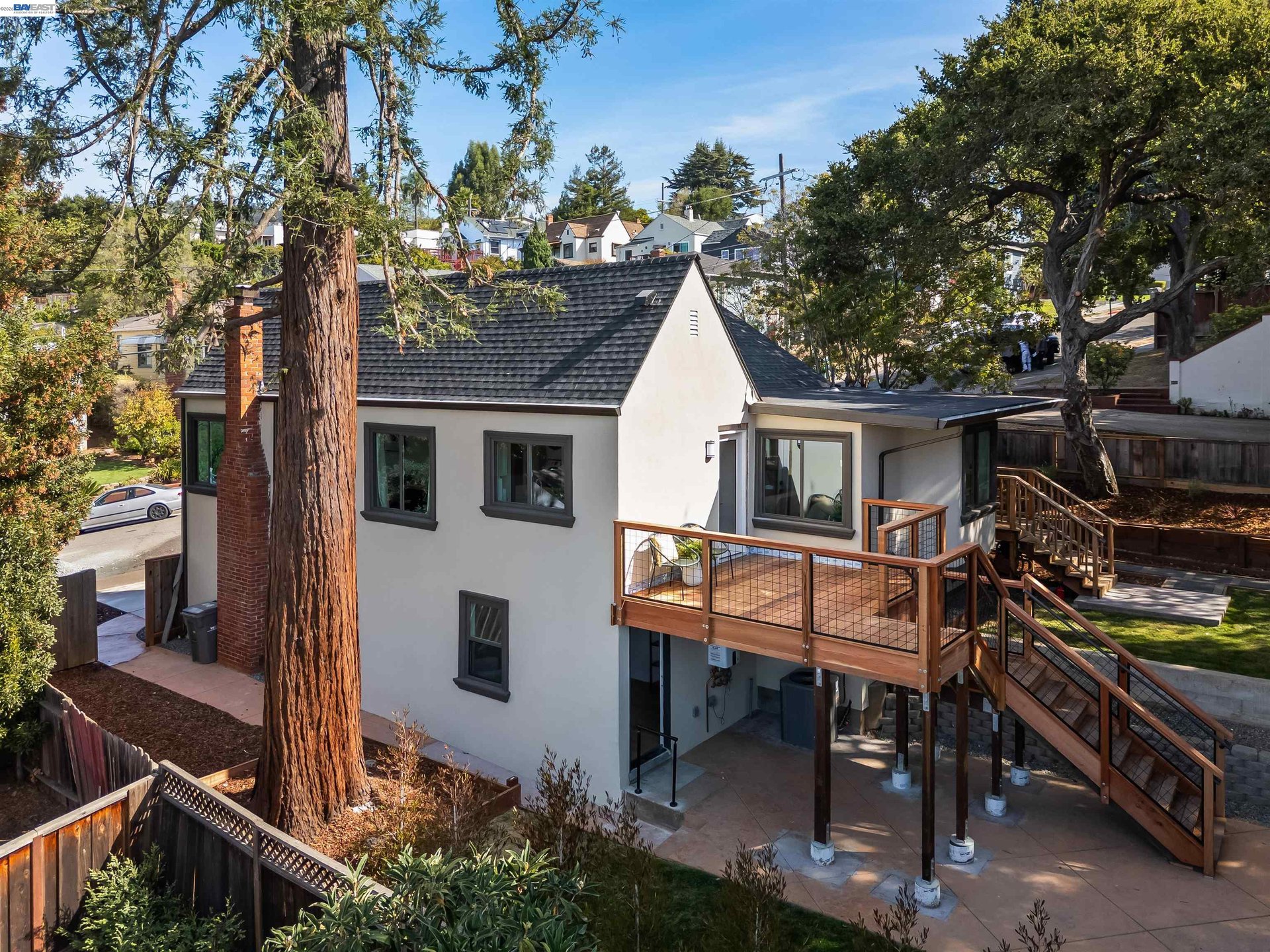 Oakland home with a raised wood deck and stairs beneath mature trees.