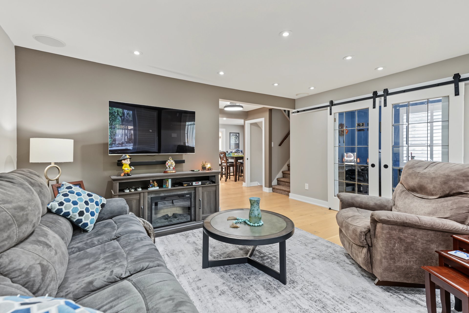 Living room with gray sofas, a round coffee table, wall-mounted television, and sliding barn-style doors.