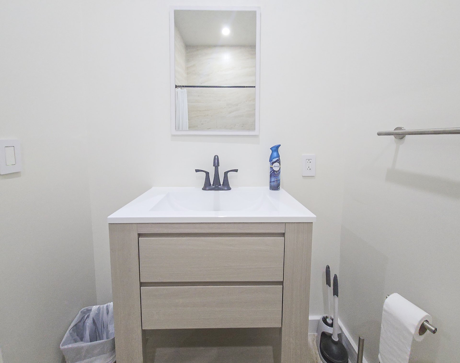 Bathroom vanity with light wood drawers, a white sink, and a dark faucet beneath a wall mirror.