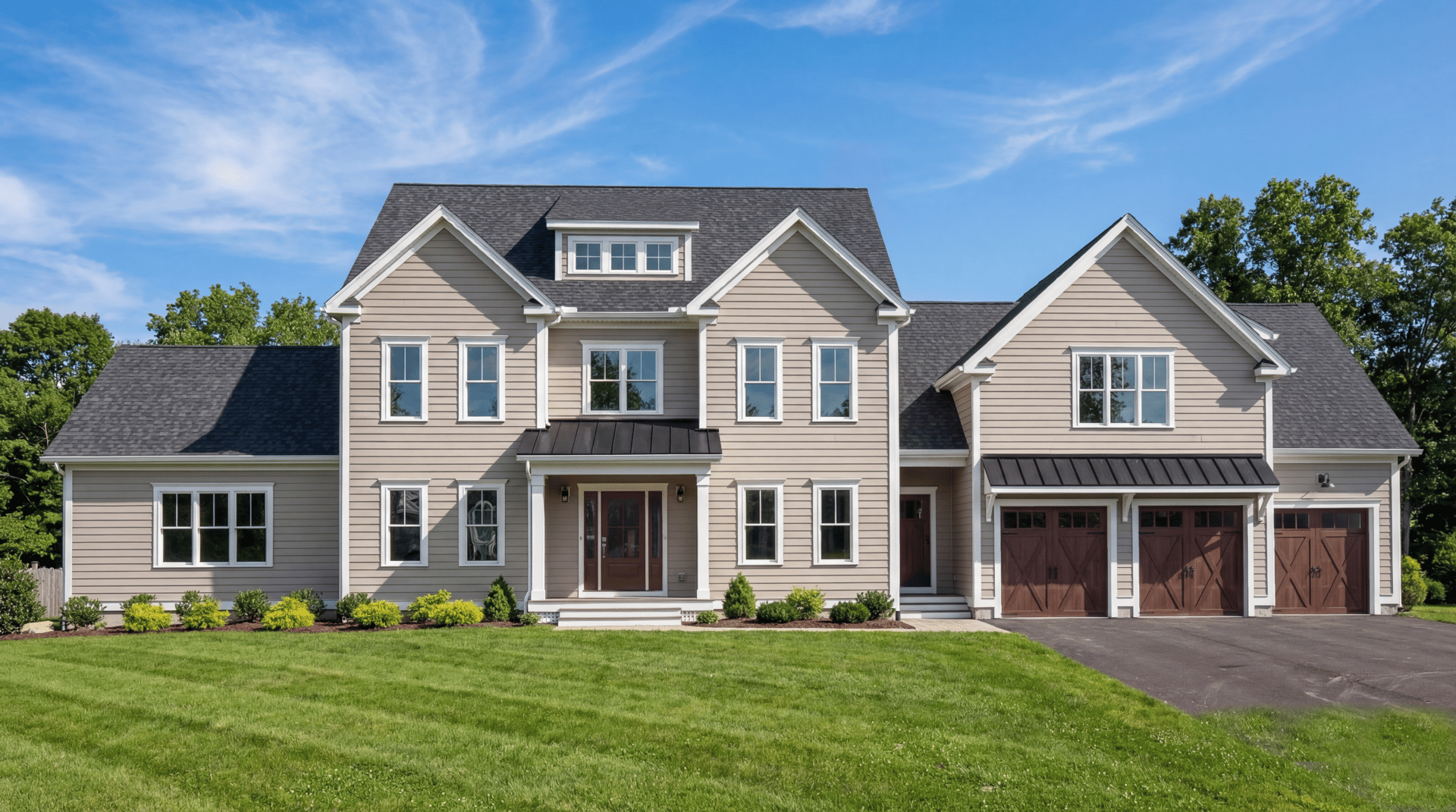 Two-story taupe house with multiple gables and a three-car garage, front view across a lawn.