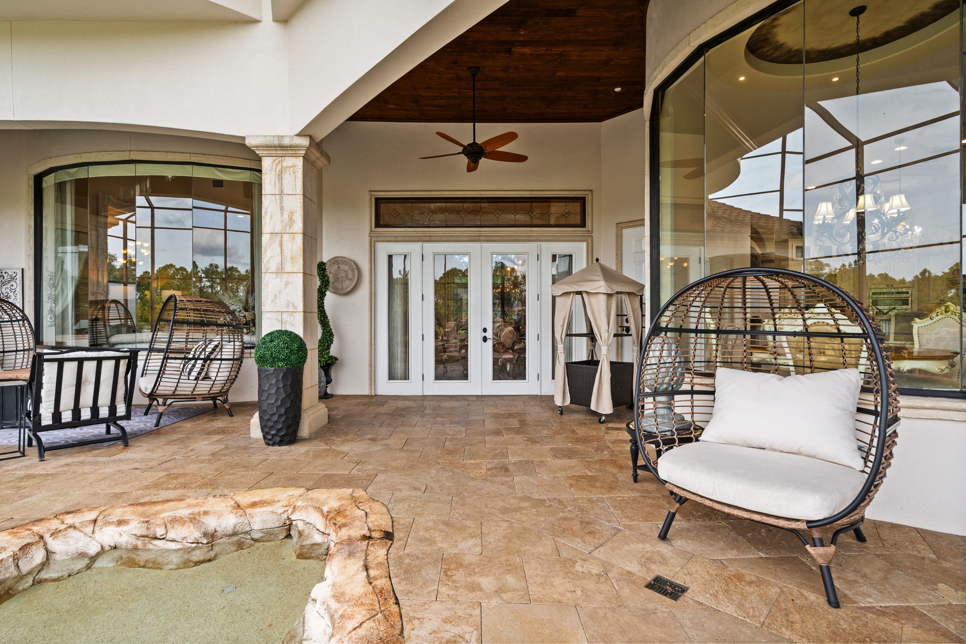 Covered patio with a small spa, wicker lounge chairs, and glass doors.