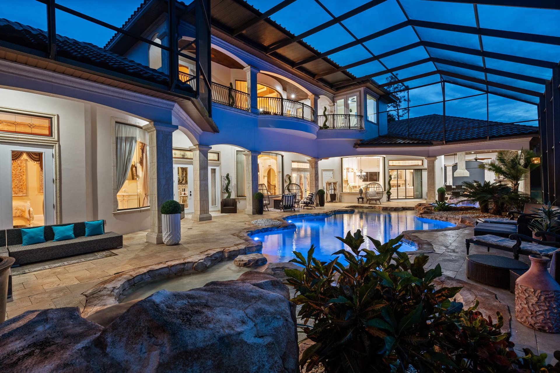 Courtyard pool at dusk, surrounded by a two-story home beneath a screened enclosure.